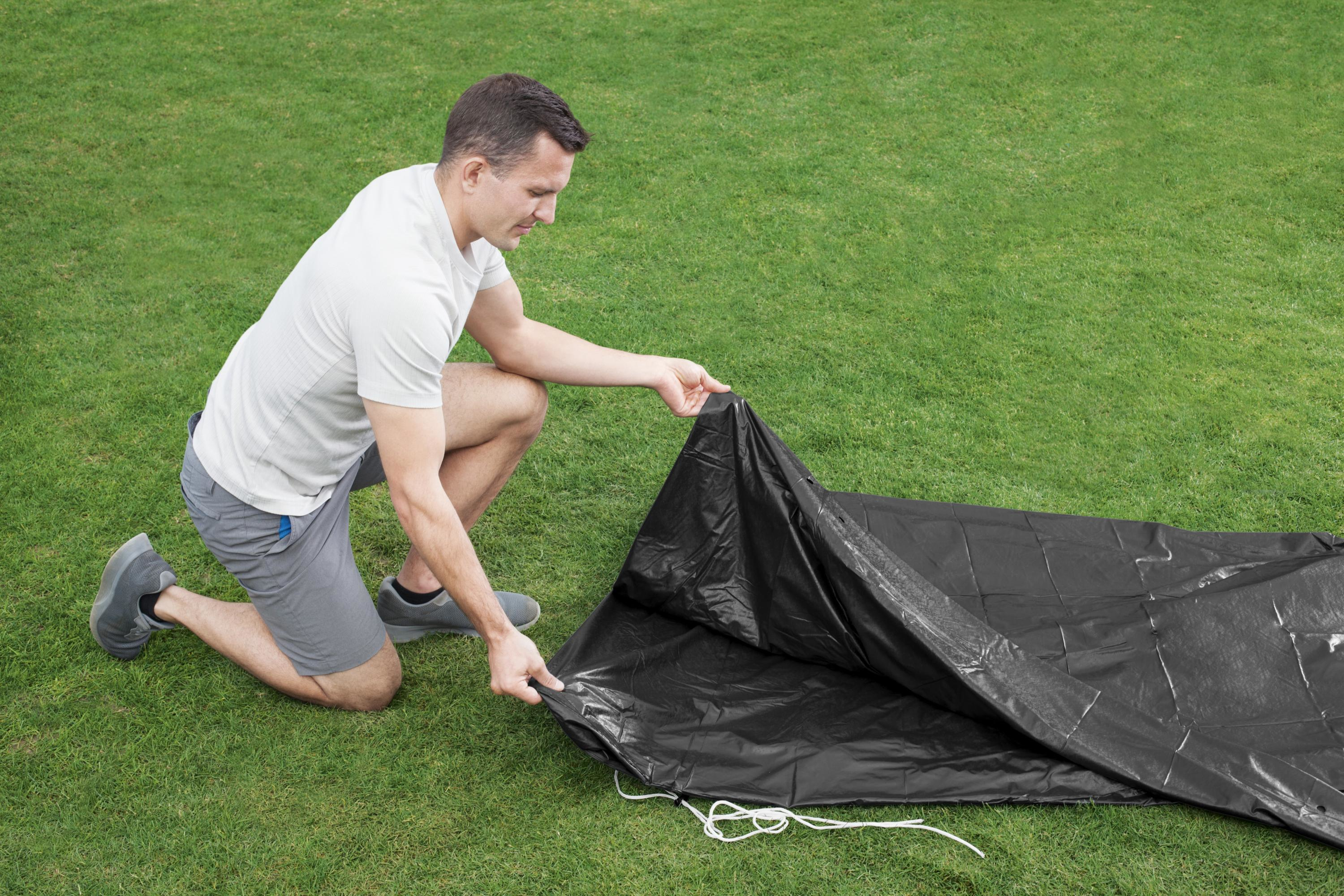Ein Mann kniet auf grünem Gras und entfaltet eine schwarze Plane.