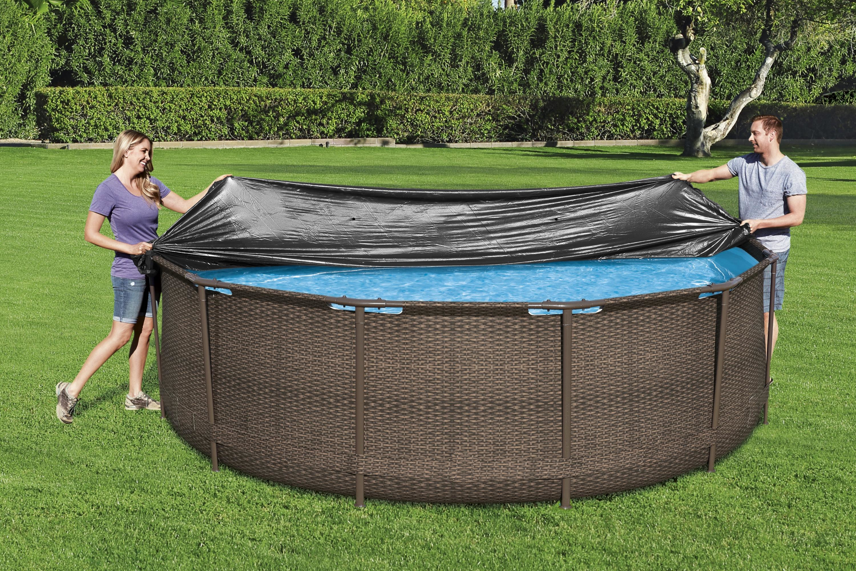 Zwei Personen bedecken einen runden Pool mit einer schwarzen Abdeckung, grüner Gras Hintergrund.