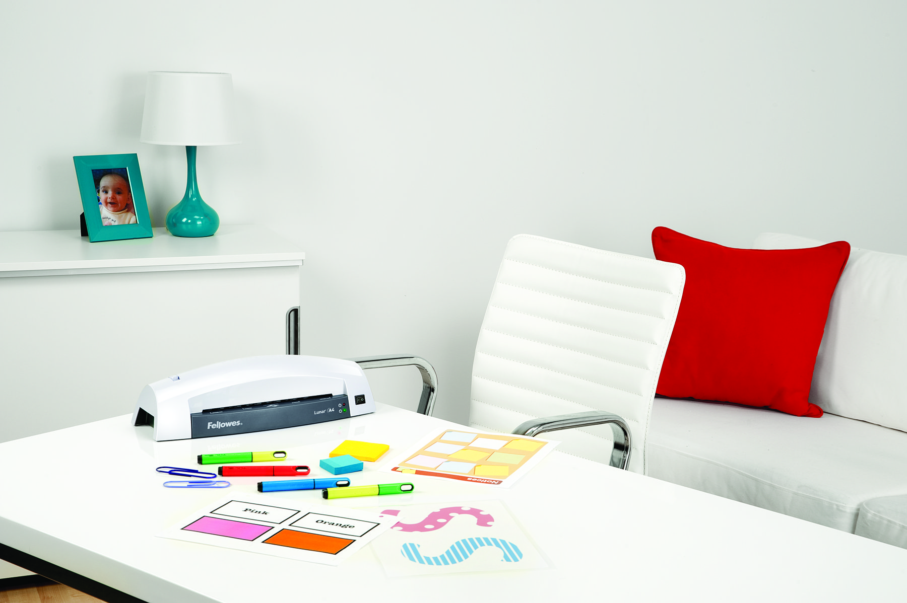 Schreibtisch mit Lampe, Drucker, Papieren und bunten Stiften.
