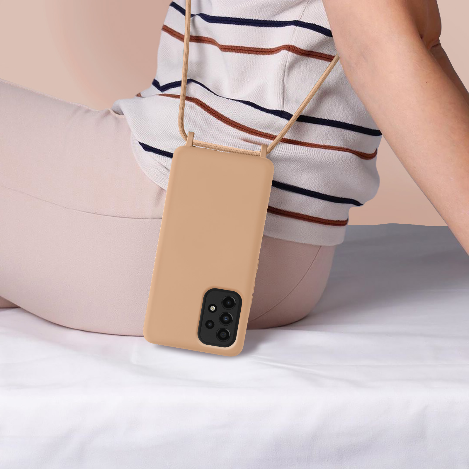 Een bruine telefoonhoes met een riem die aan het lichaam van een persoon hangt. Een persoon zit op een wit oppervlak.