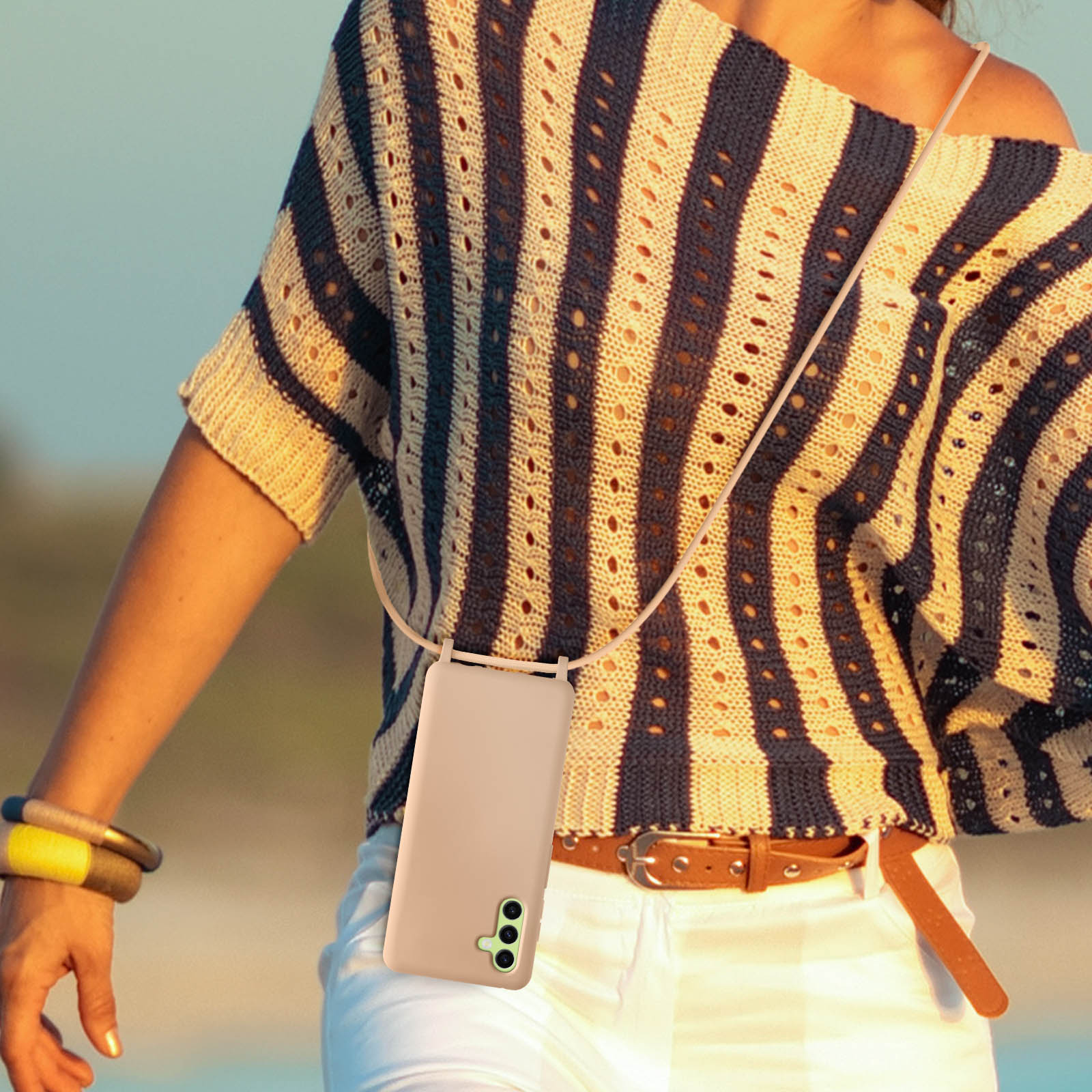Donna con custodia per telefono con cinturino. Indossa una camicia a righe e ride. Giorno di sole.