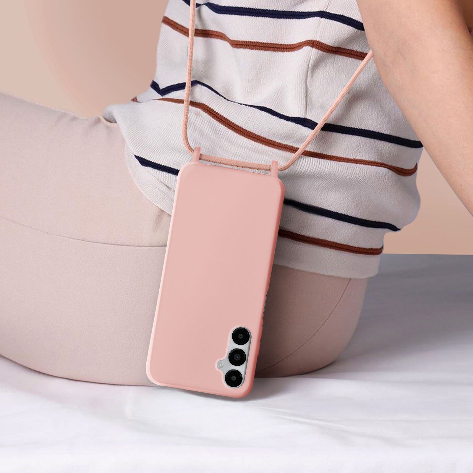 Une personne tenant un téléphone rose avec un cordon. La personne est assise sur fond blanc.