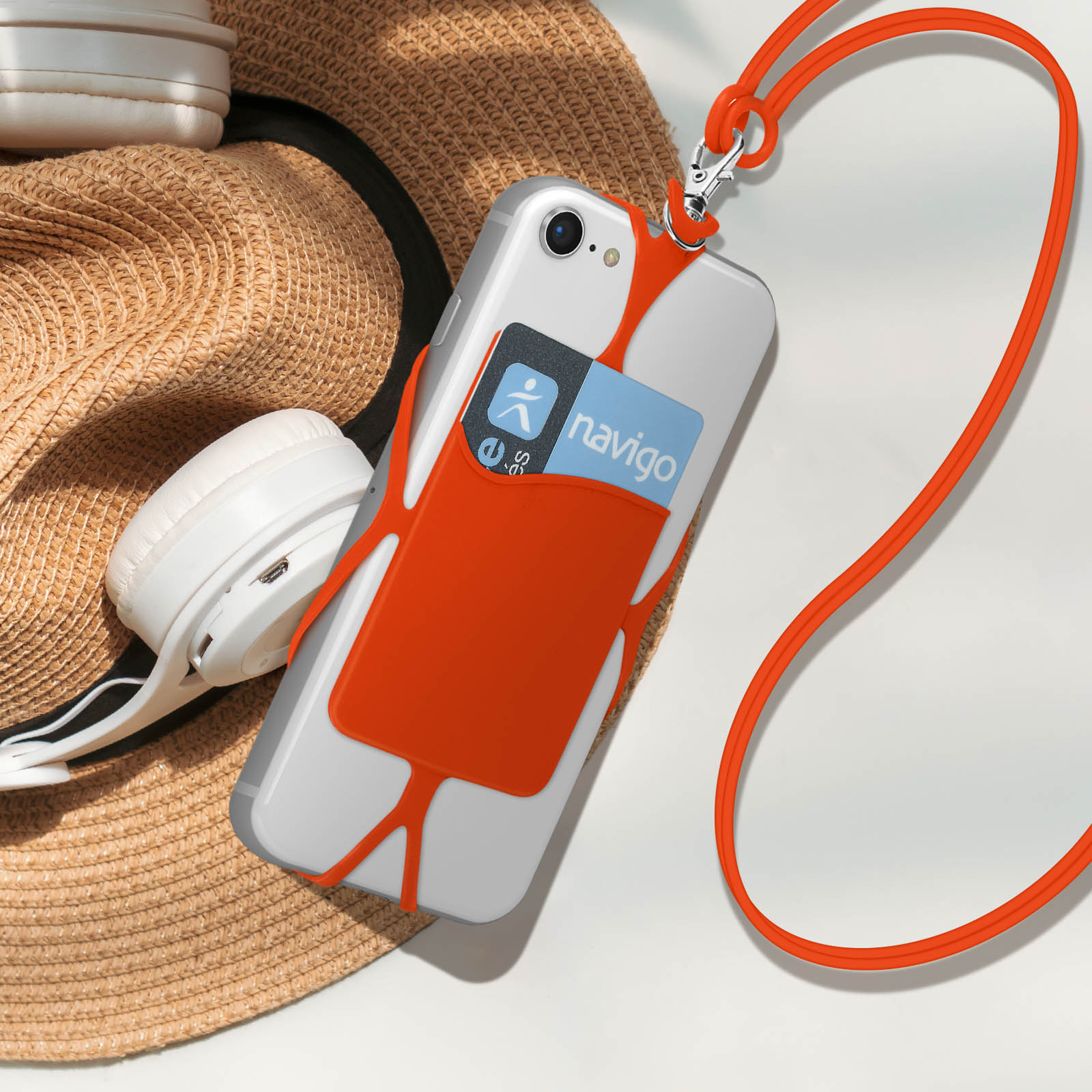 Un telefono con cinturino arancione e porta carte, con cappello e cuffie sullo sfondo.