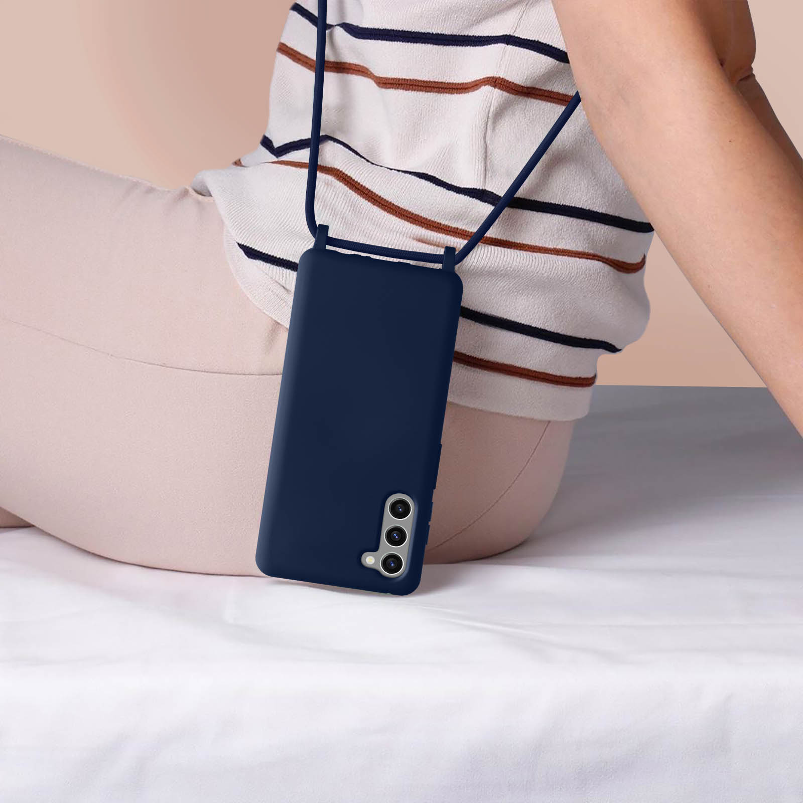 Personne portant chemise rayée blanche et marron tenant un téléphone sur draps blancs.
