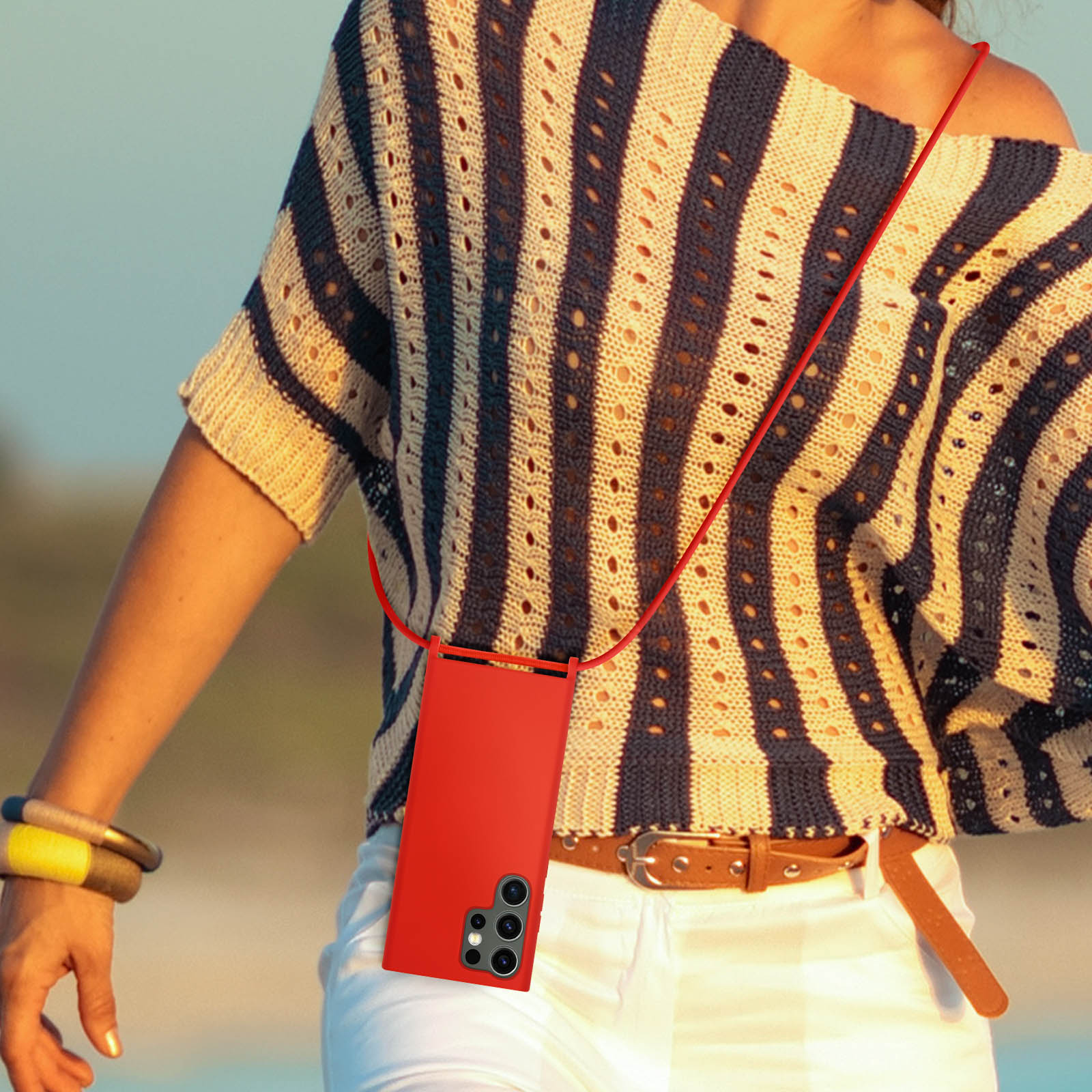 Una donna indossa una collana con custodia rossa per telefono. Pantaloni bianchi e camicia a righe.