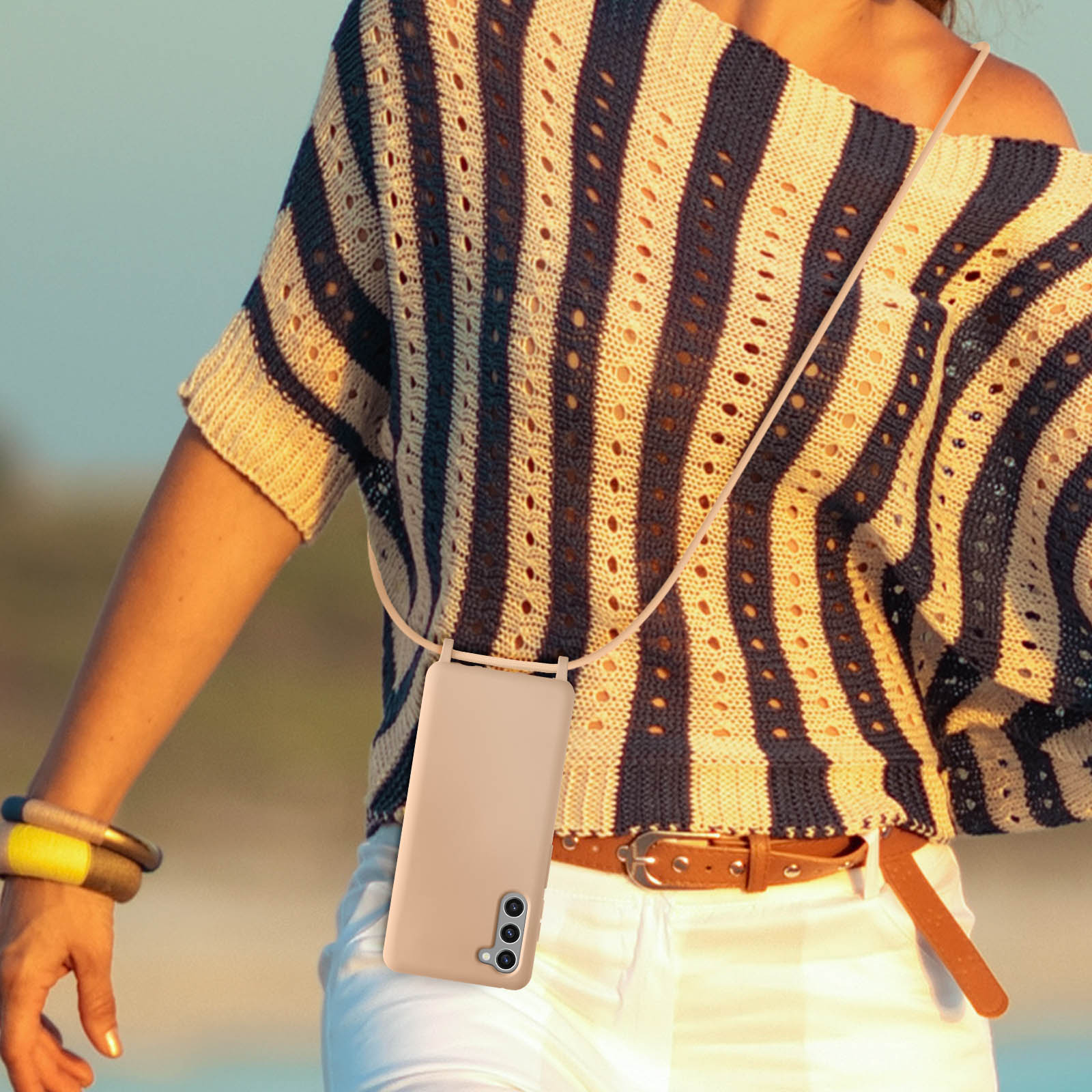 Una custodia per telefono beige con un cordino, indossata da una persona sulla spiaggia.