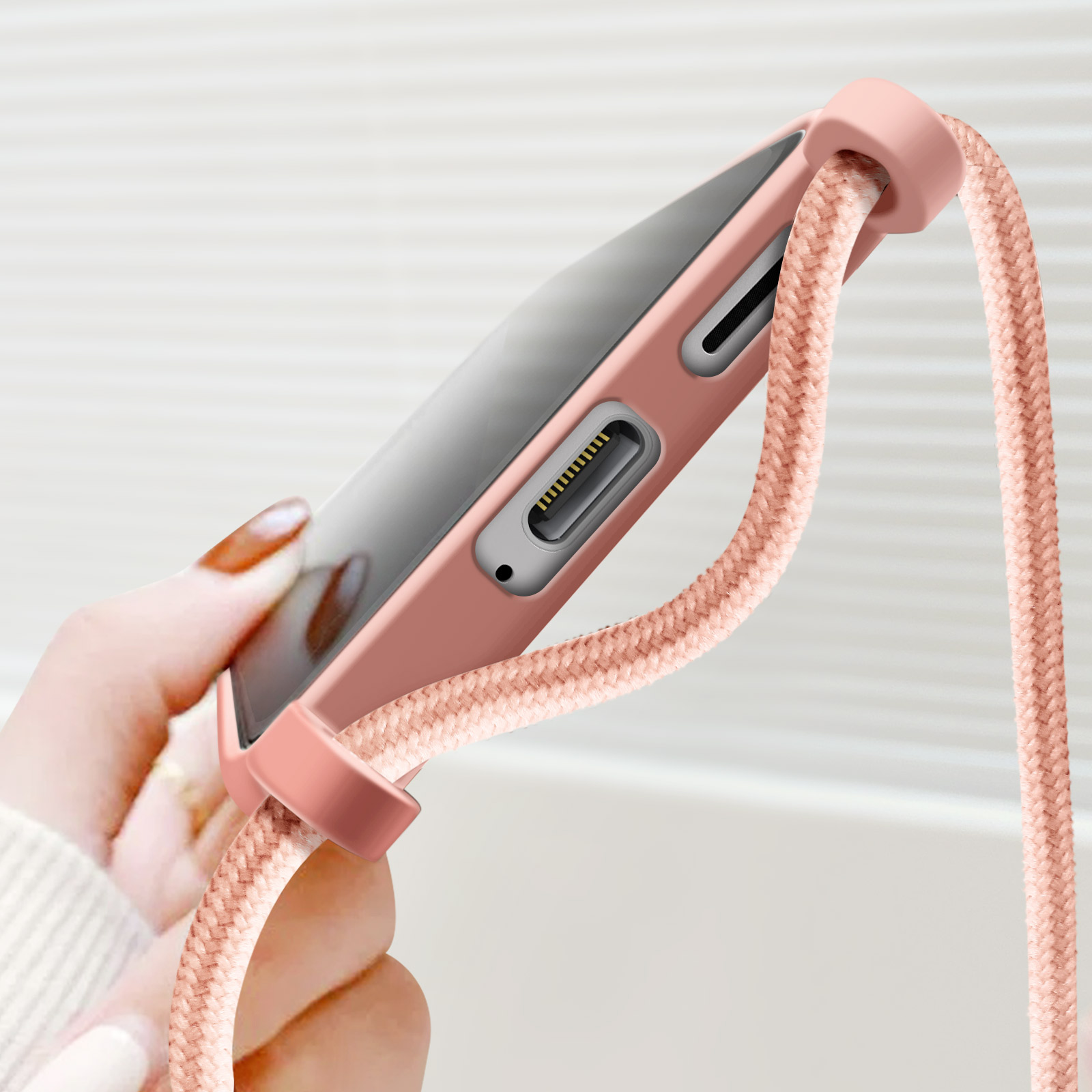 Custodia per telefono rosa con cordino. Una mano tiene il telefono. Sfondo sfocato.
