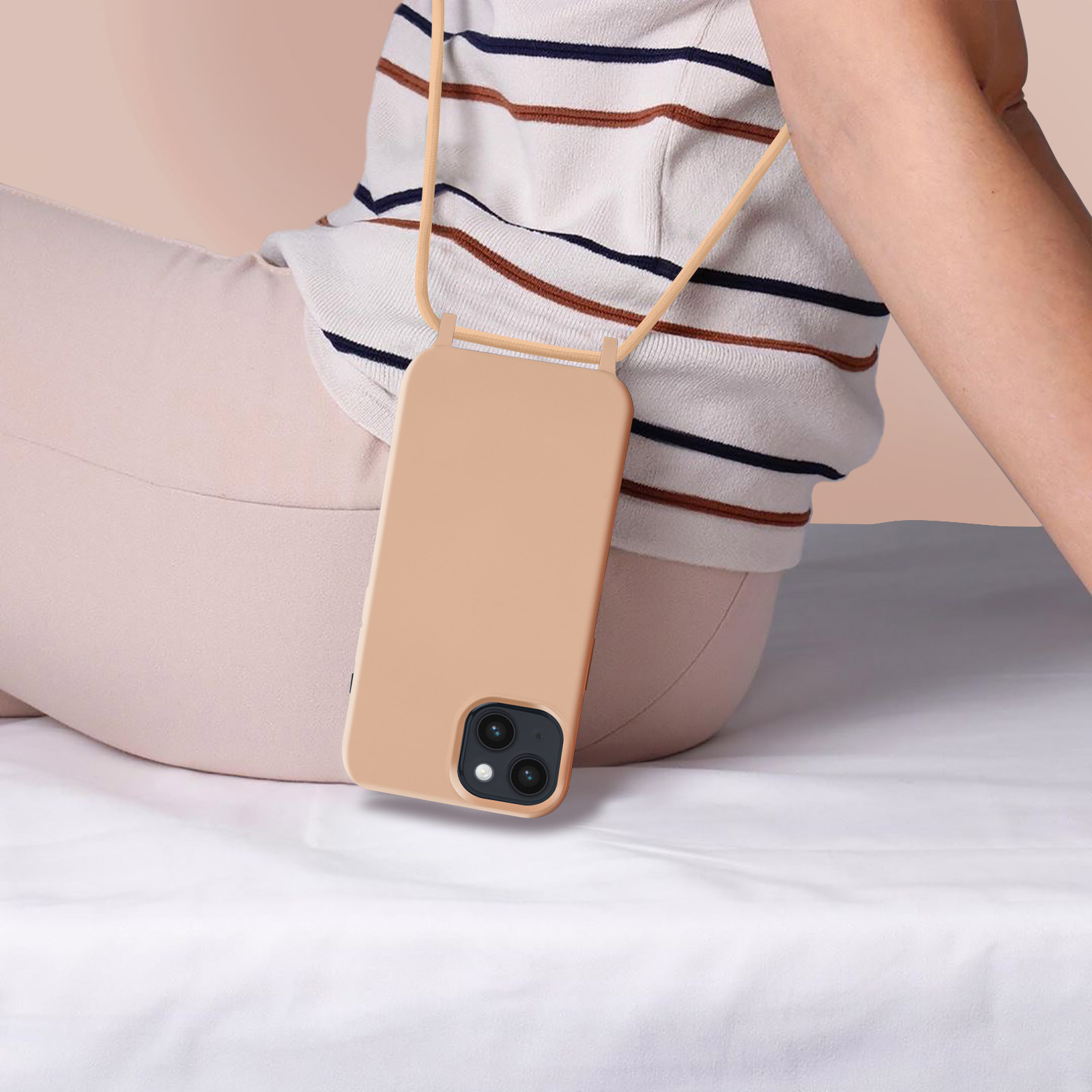Een persoon draagt een telefoonhoesje met een beige bandje, zittend op een bed. Witte achtergrond.