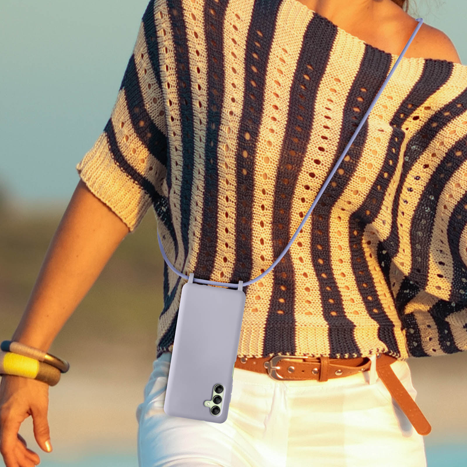 Donna con camicia a righe, collana con custodia lavanda, pantaloni bianchi e cintura marrone.