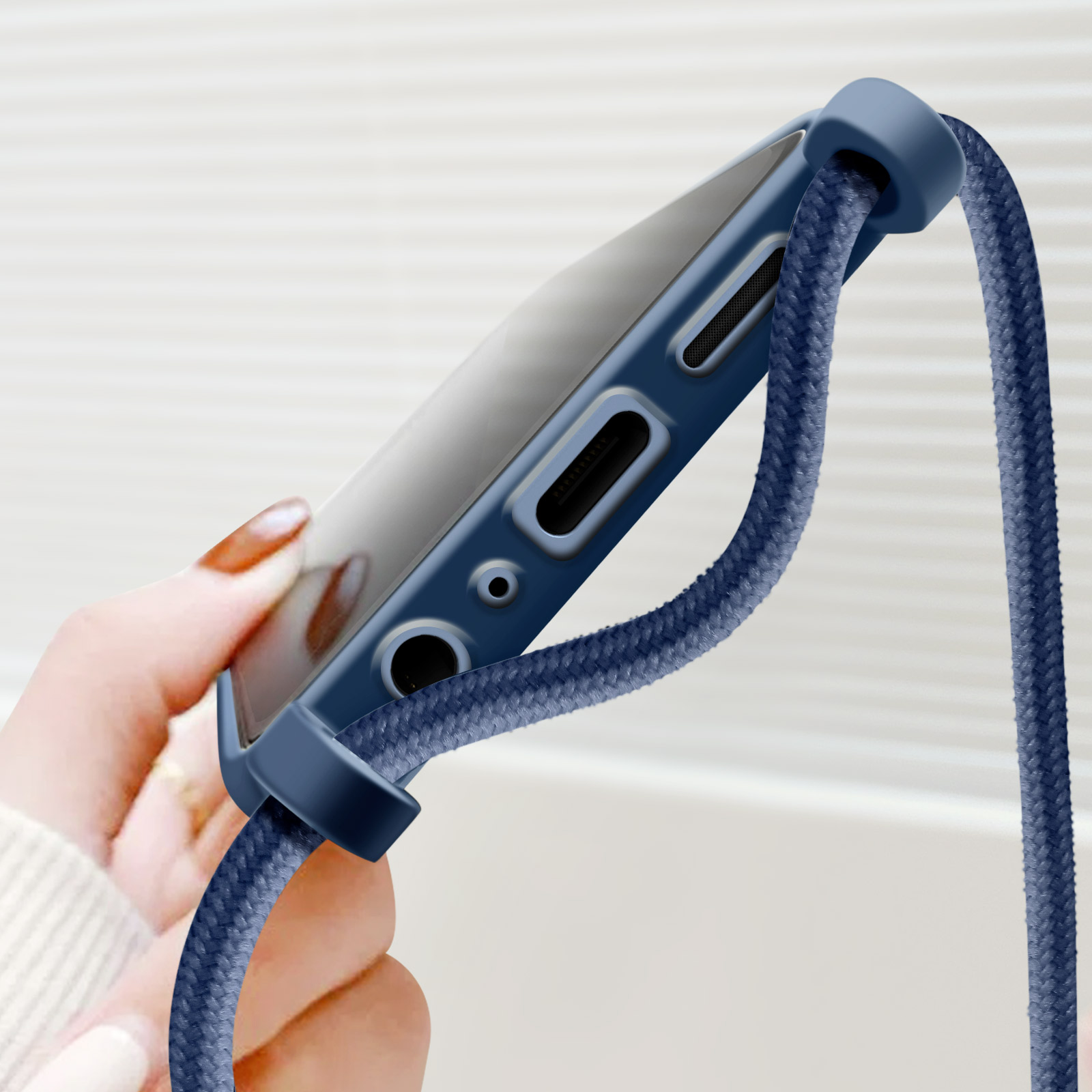 Una custodia per telefono blu con un cordino attaccato. Una mano tiene il telefono. La custodia e il cordino sono blu.
