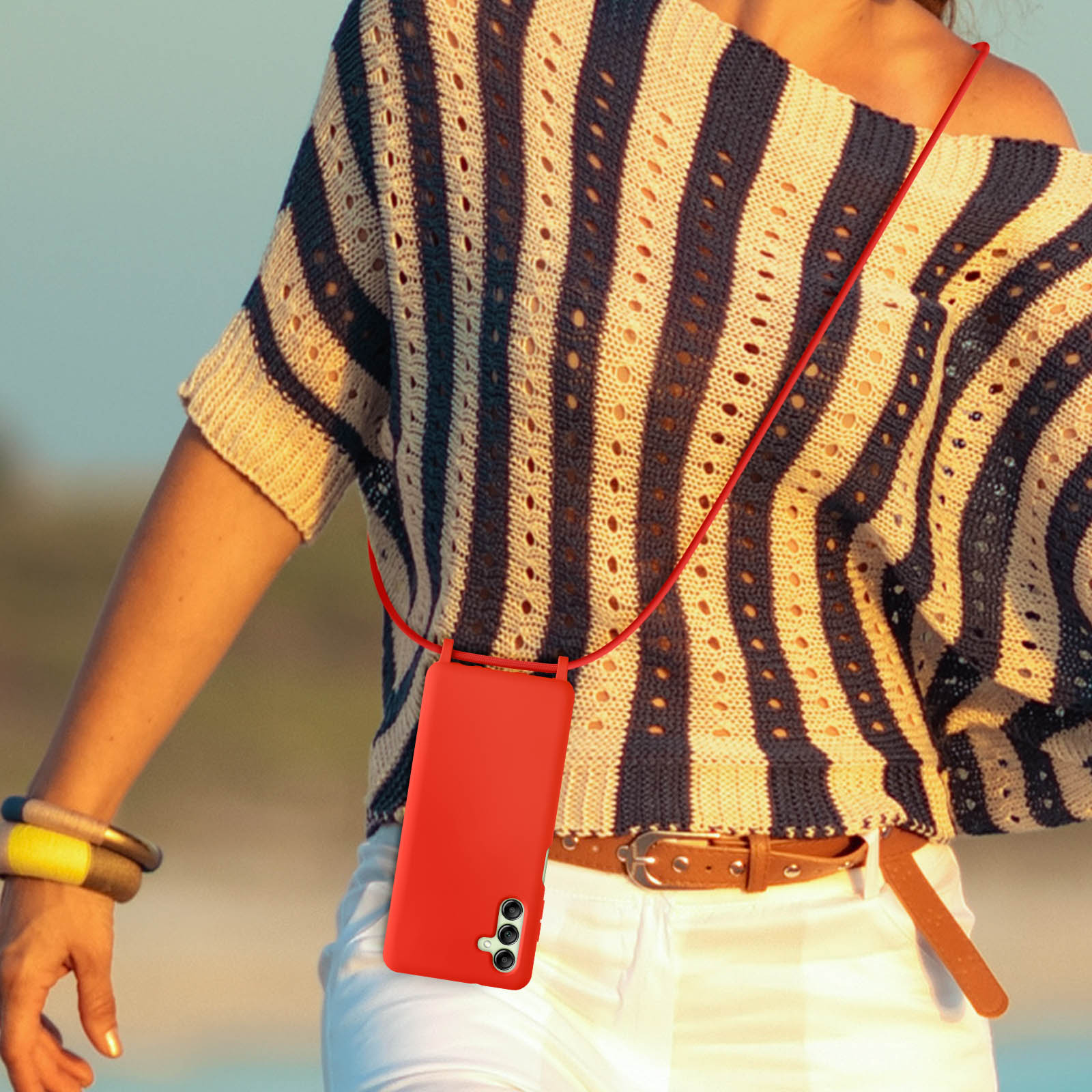 Donna con custodia rossa su cordino rosso. Pantaloni bianchi, camicia a righe.