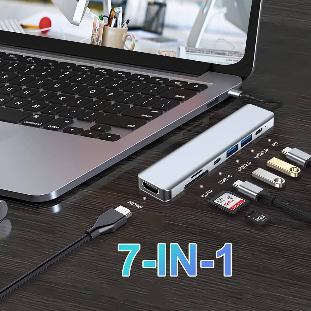 Silberner 7-in-1 USB-C Hub, der an einen Laptop angeschlossen ist, mit verschiedenen Anschlüssen und Zubehör.