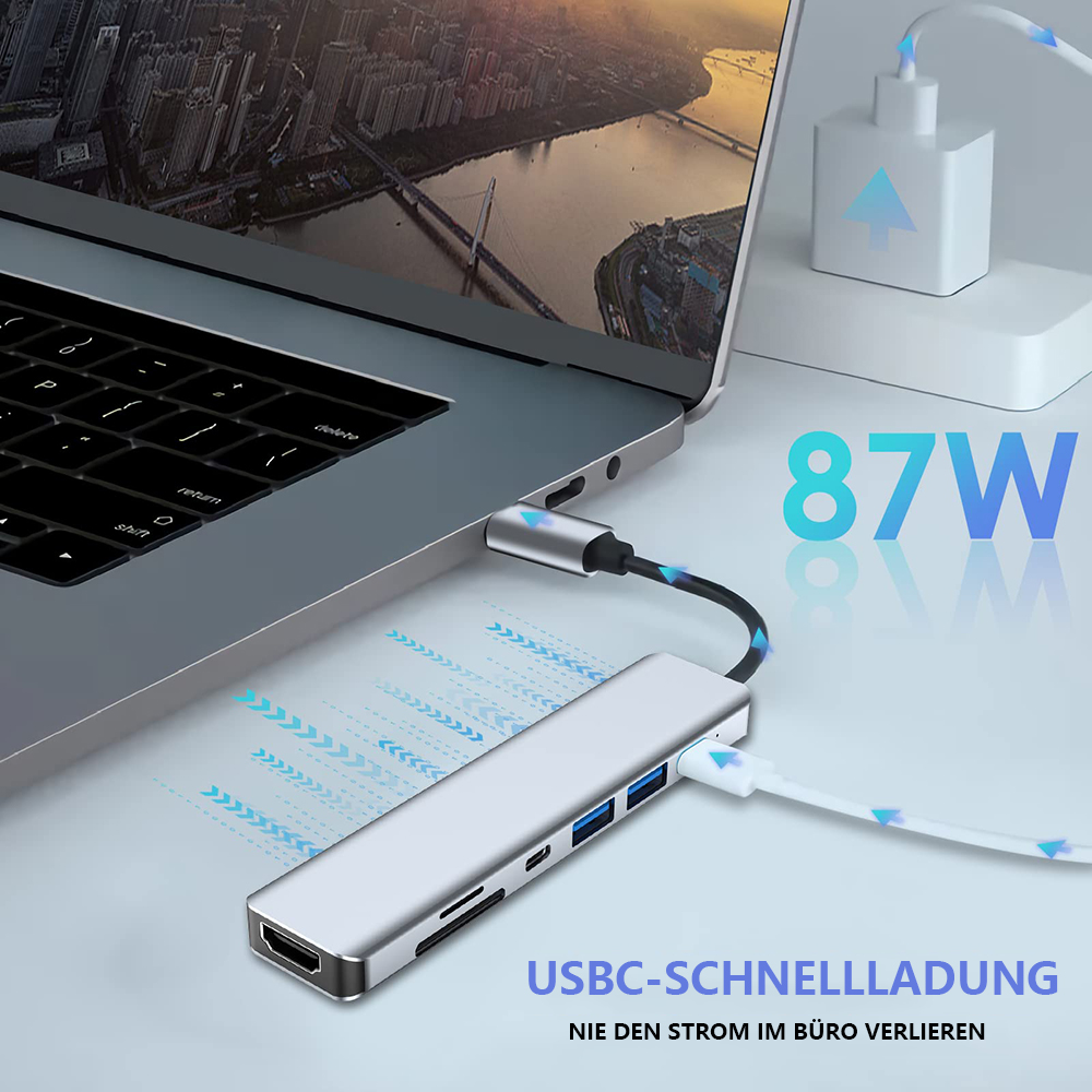Ein Laptop ist mit einem silbernen USB-C-Hub mit 87W-Etikett und Ladekabel verbunden.