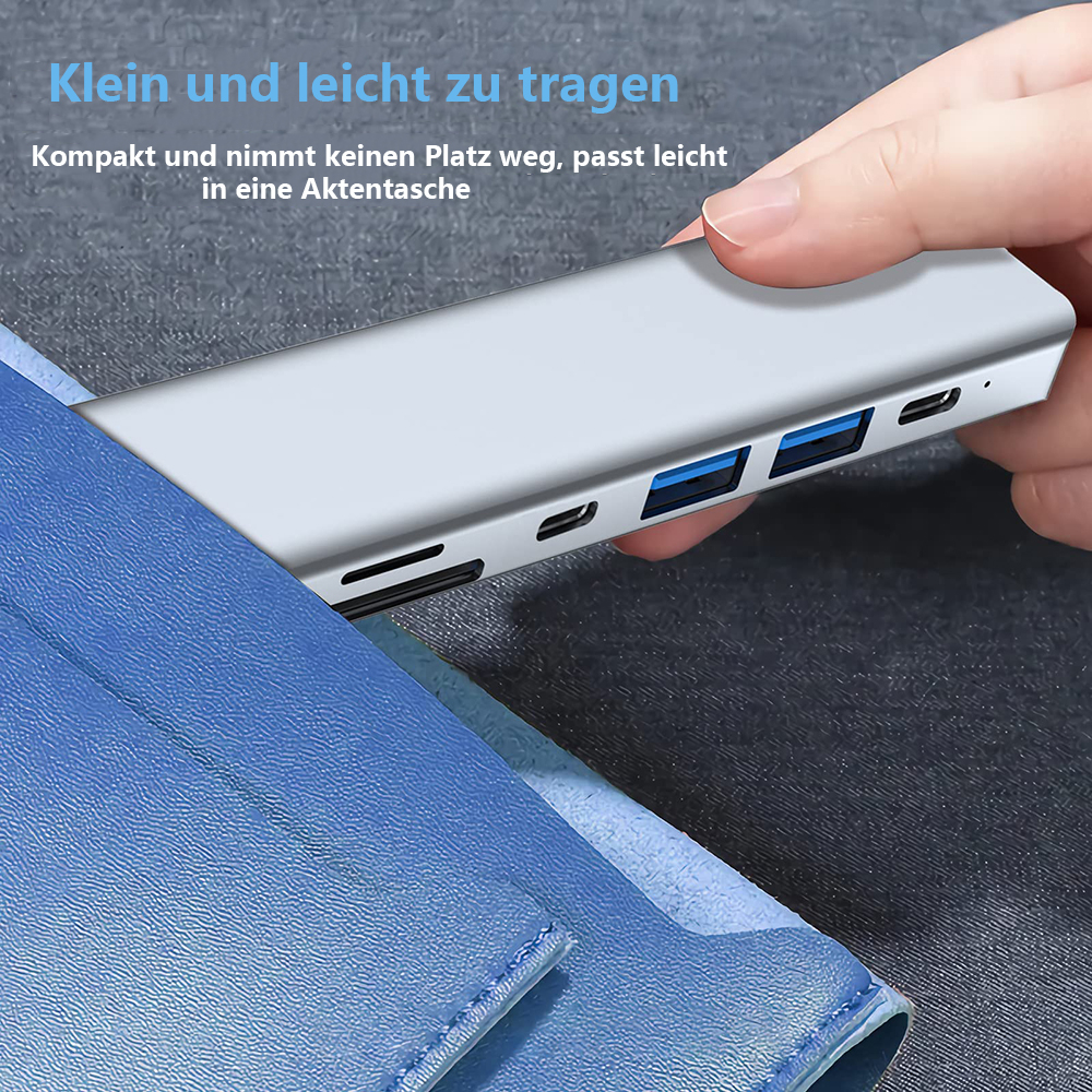 Hand hält einen silbernen USB-Hub über einem blauen Notizbuch. Mehrere USB-Anschlüsse sind sichtbar.