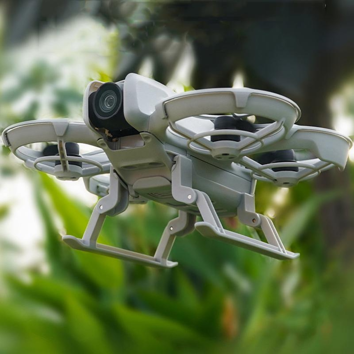 Un drone grigio chiaro con quattro eliche è in volo su uno sfondo verde sfocato.