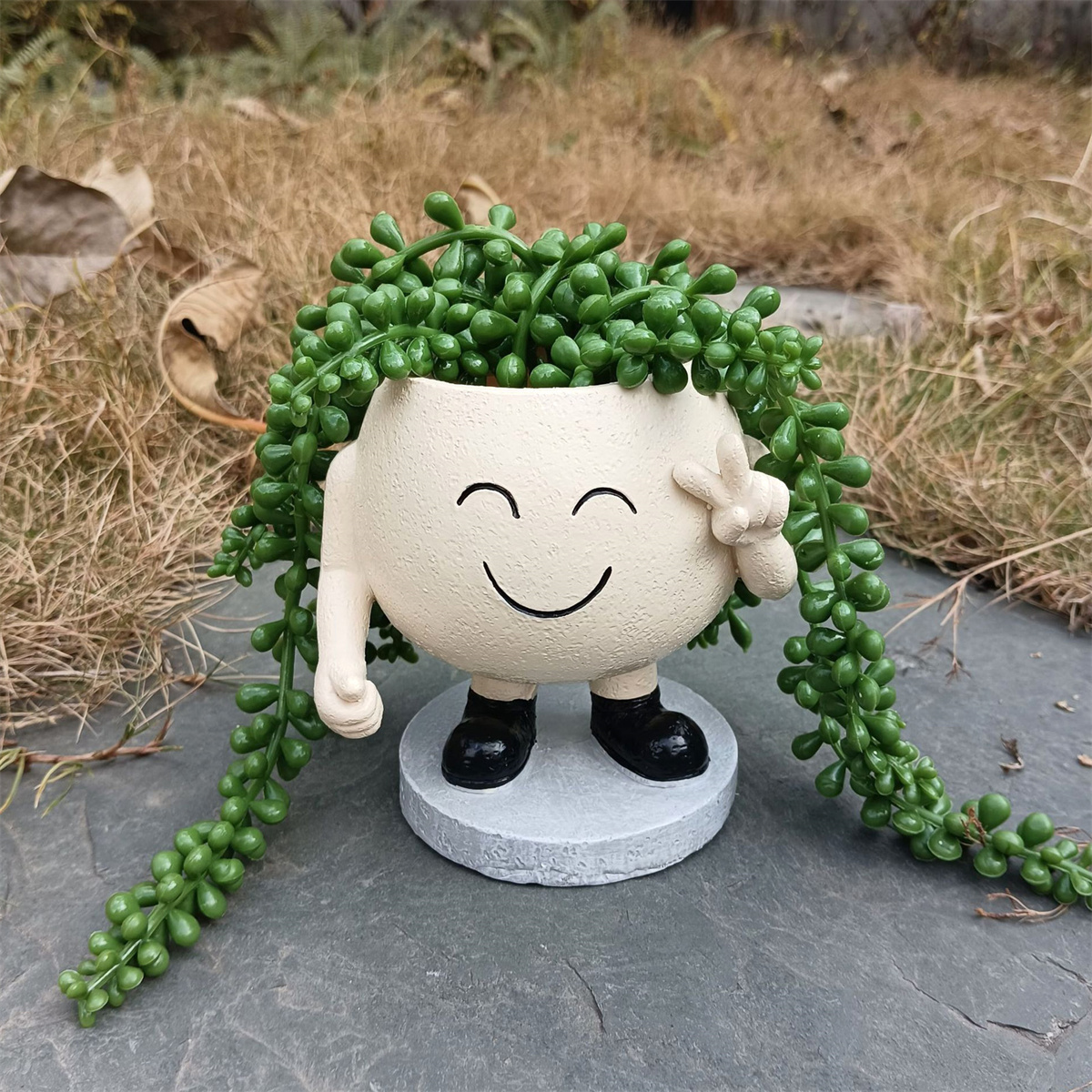 Ein fröhlicher, lächelnder Topf in Form eines Gesichts, der ein Friedenszeichen hochhält. Grüne Pflanze wächst aus dem Topf.