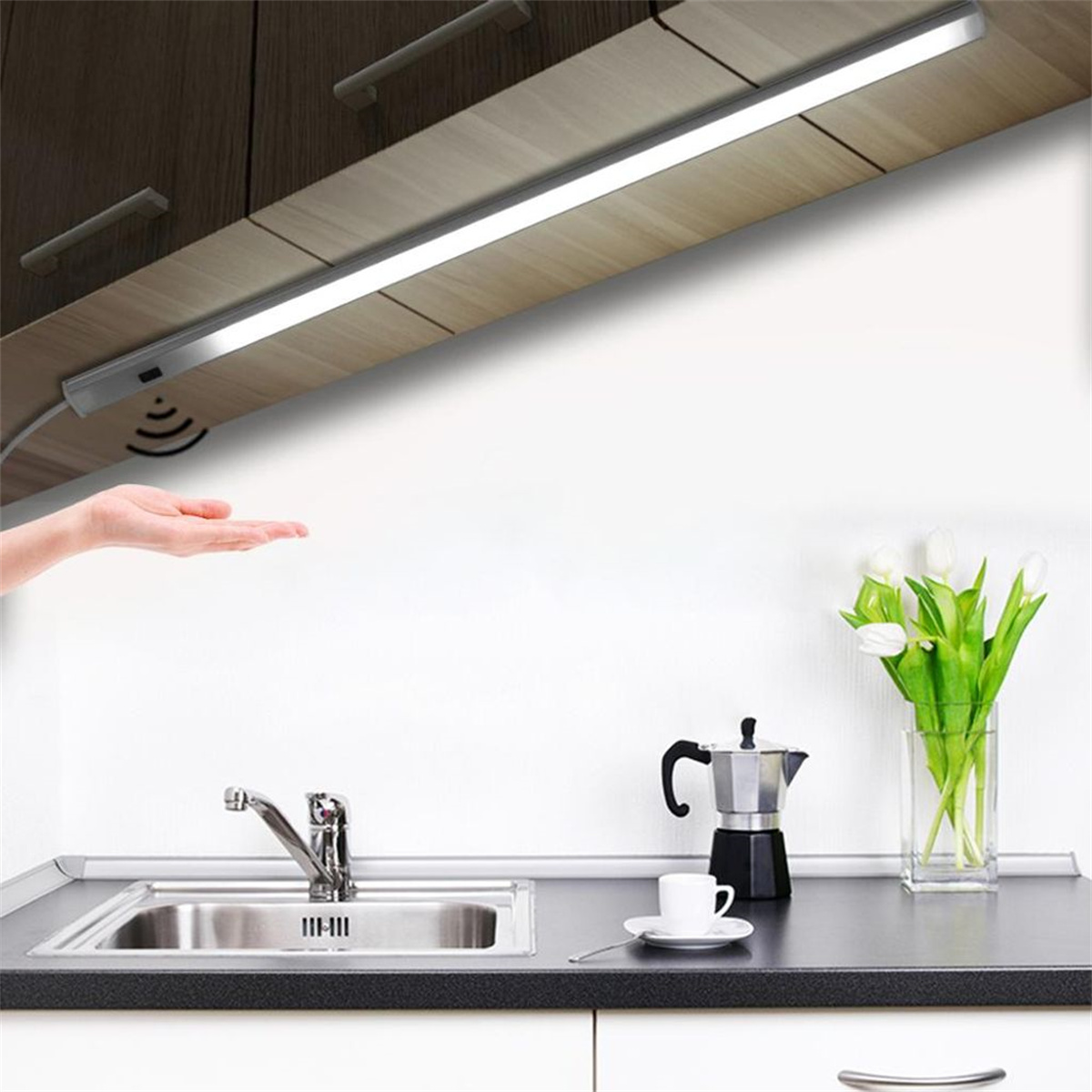 Küchenszene mit Licht unter einem Schrank. Eine Hand greift nach einem Sensor. Blumen und Kaffeemaschine.
