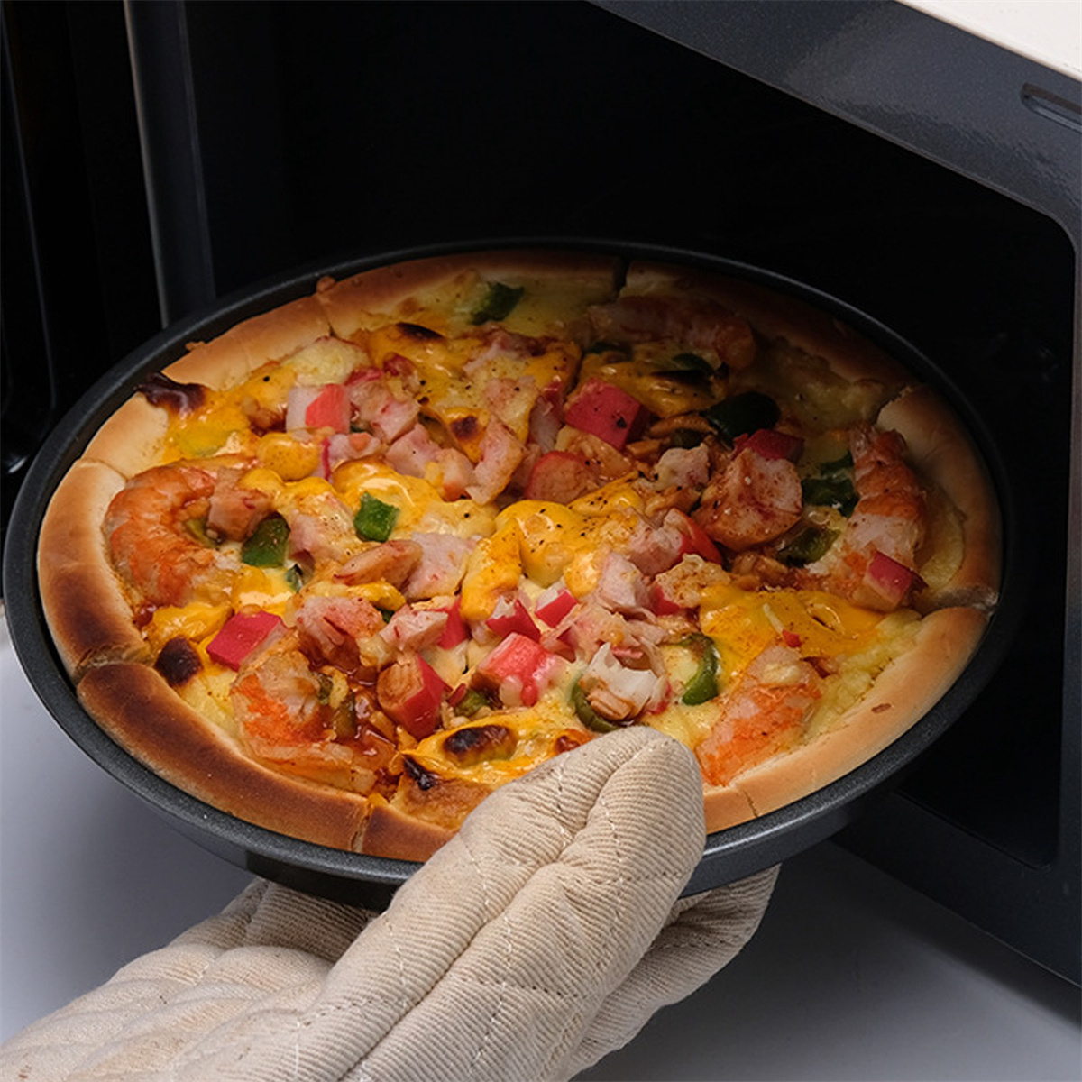 Pizza in einer Pfanne, wird aus einem Ofen genommen. Die Pizza hat Beläge und geschmolzenen Käse.
