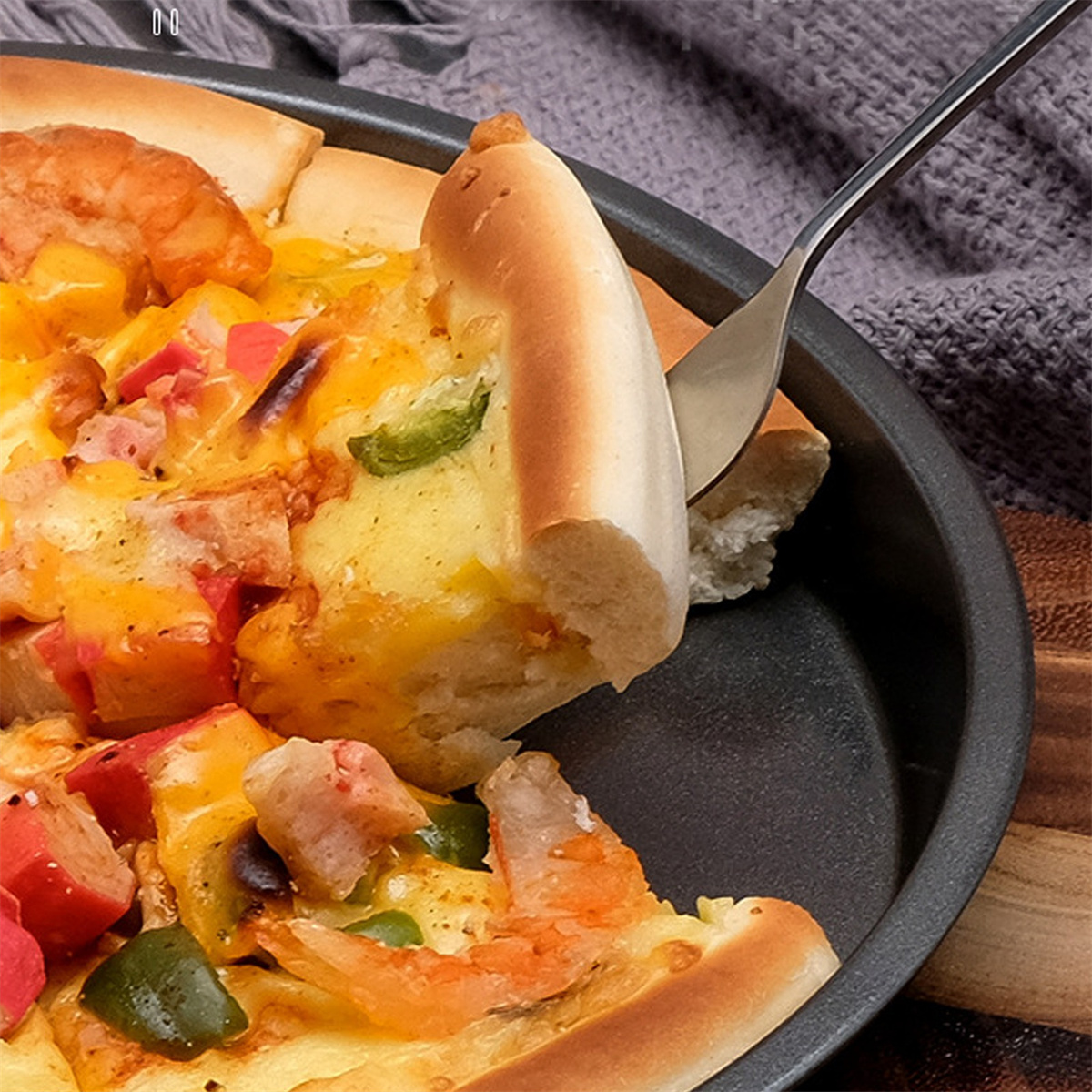 Pizzastück wird aus einer Pfanne gehoben. Die Pizza hat verschiedene Beläge und einen fluffigen Rand.
