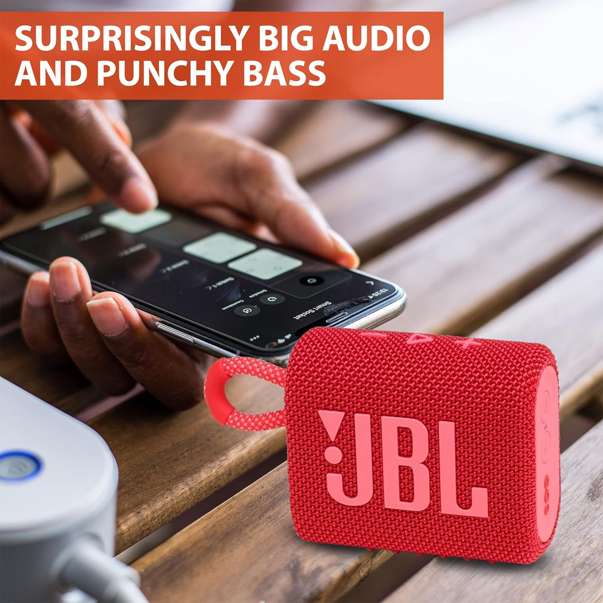 Roter JBL-Lautsprecher mit einer Person, die ein Telefon hält, auf einem Holztisch.