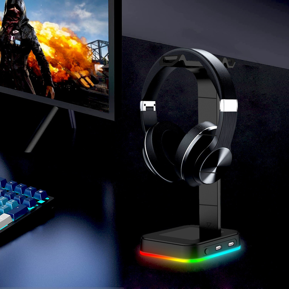 Kopfhörer auf einem schwarzen Ständer mit farbigen LED-Leuchten. Eine Tastatur und ein Monitor befinden sich im Hintergrund.
