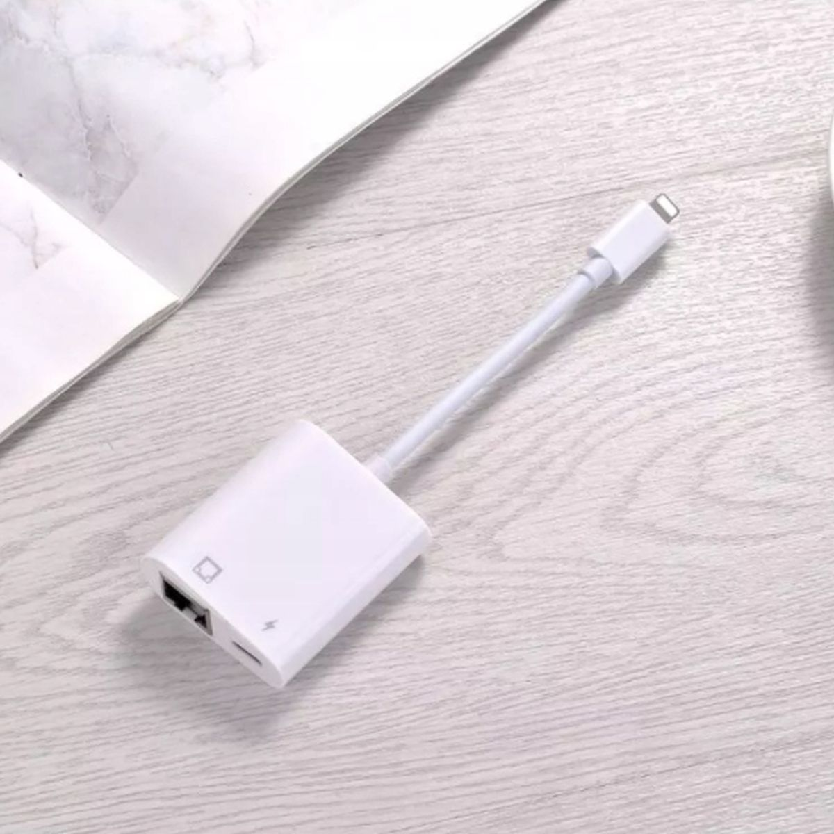 Biały adapter ze złączem Lightning i portem USB, umieszczony na jasnej drewnianej powierzchni.