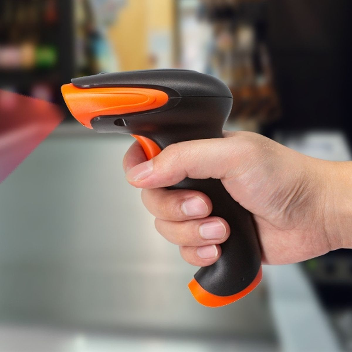 Dłoń trzymająca czarno-pomarańczowy skaner kodów kreskowych.