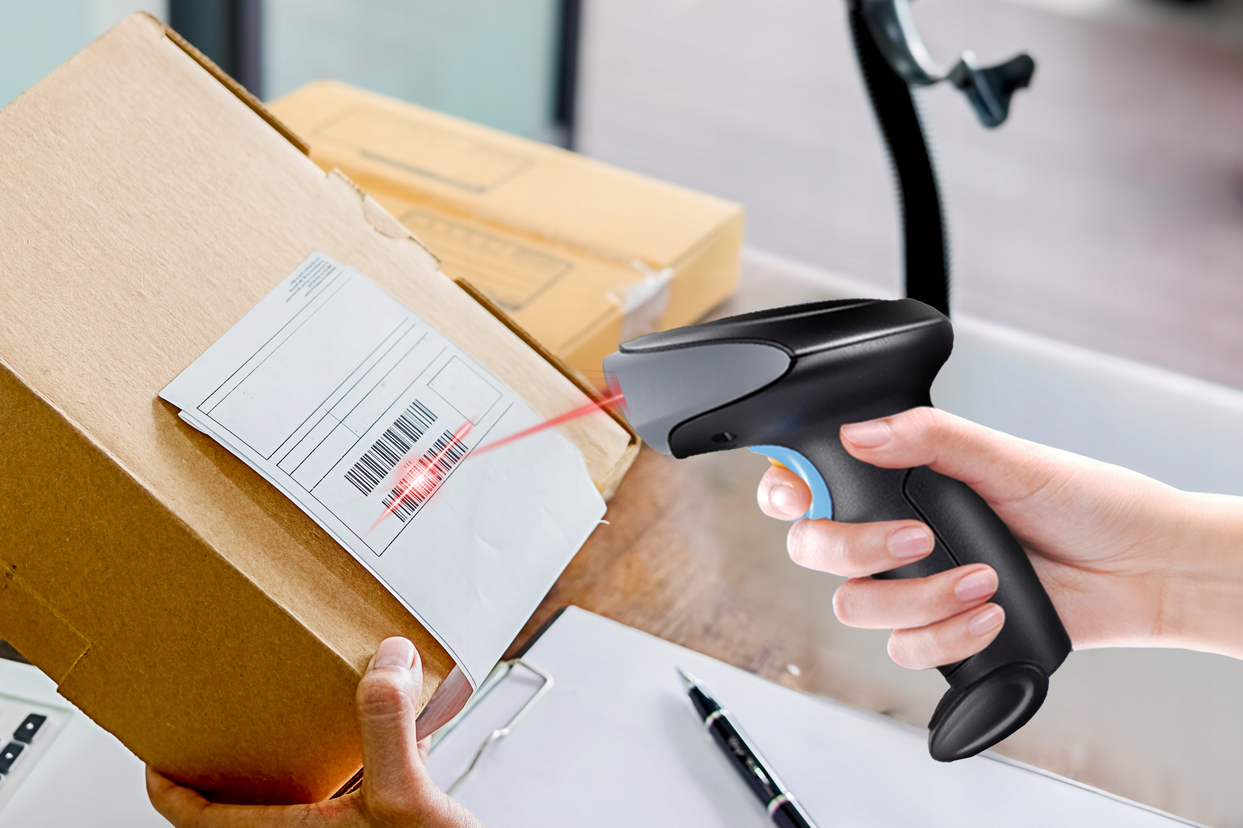 Osoba skanująca kod kreskowy na kartonie za pomocą czarno-niebieskiego skanera.