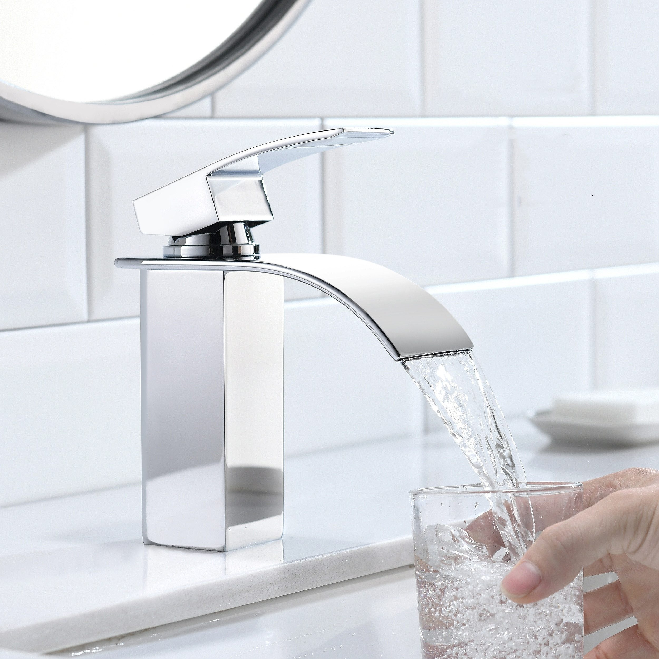 Eine verchromte Armatur, aus der Wasser in ein Glas gießt. Eine Hand hält das Glas.