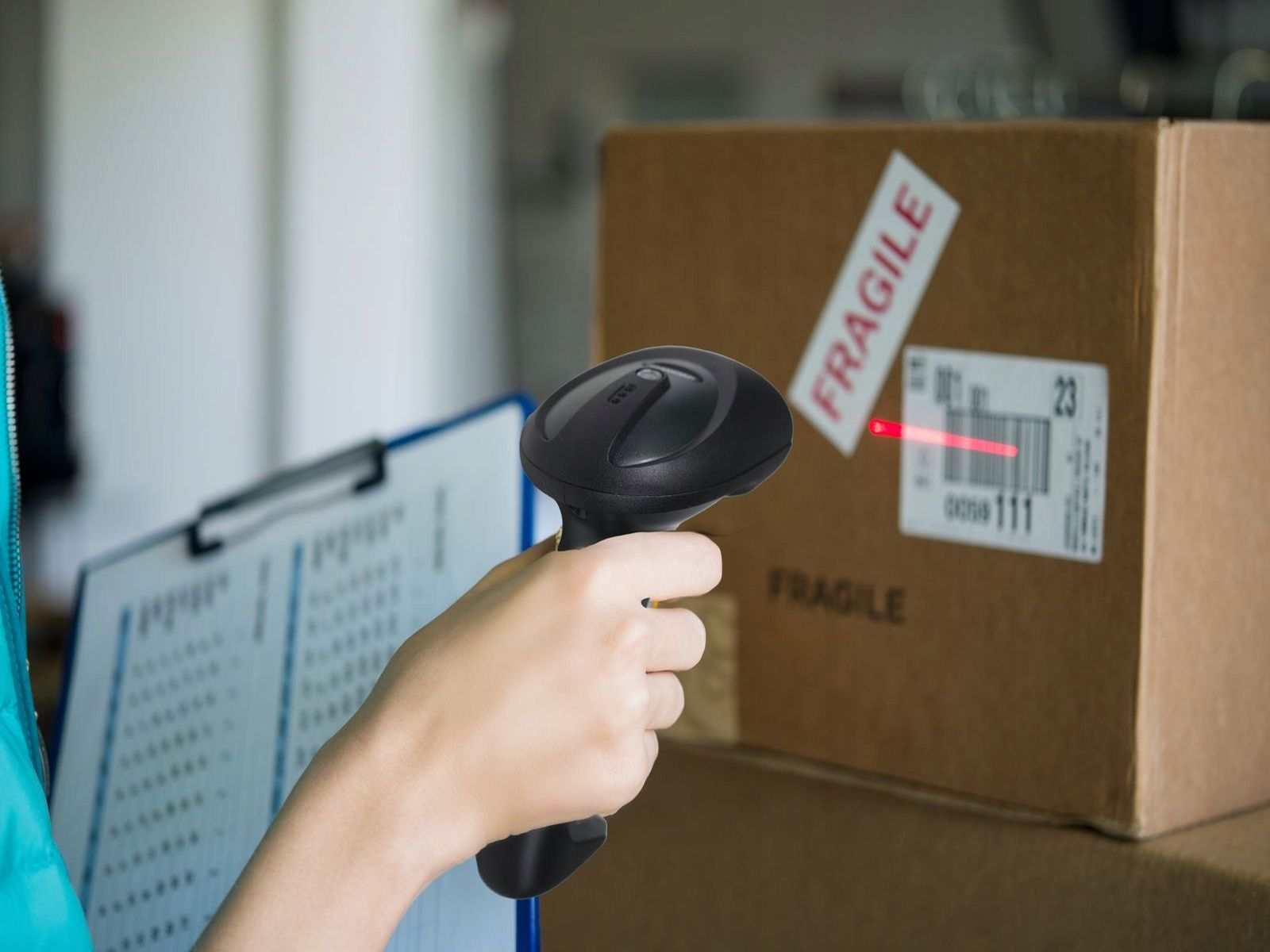 Osoba skanuje kod kreskowy na pudełku za pomocą czarnego skanera. Pudełko ma naklejkę 'Fragile'.