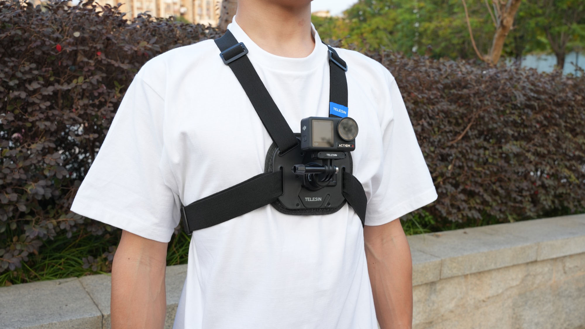 A person wearing a chest strap with a camera attached, standing outside.