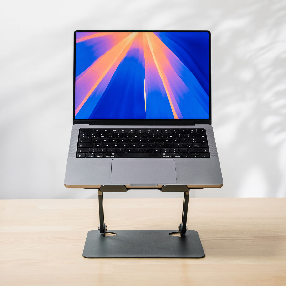 Un laptop aperto su un supporto su un tavolo di legno. Lo sfondo è un muro bianco.