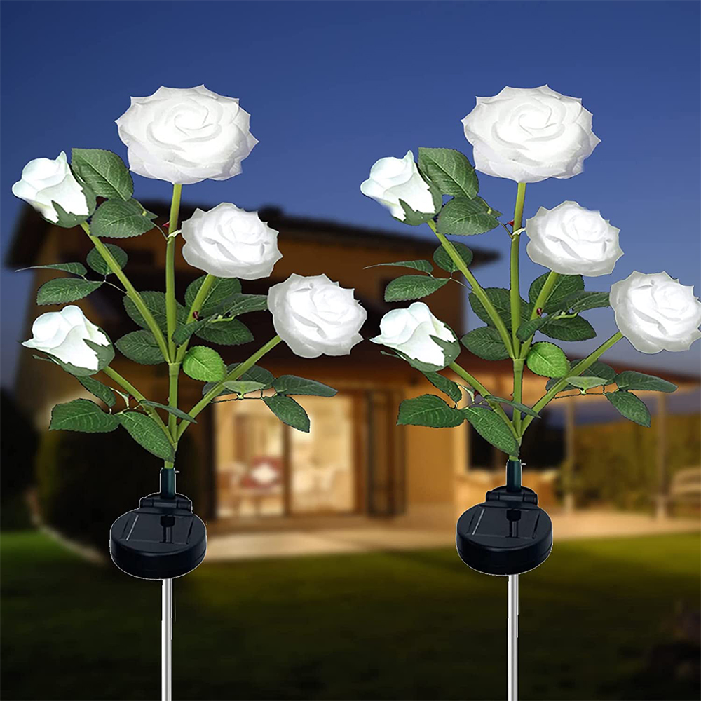 Zwei solarbetriebene, weiße Rosenblütenlichter vor einem Haus in der Dämmerung.