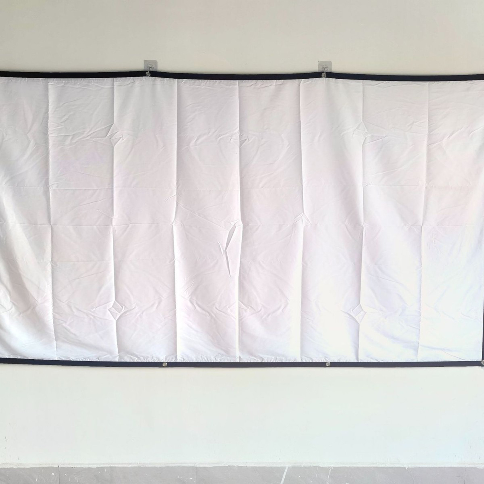 Weiße Projektionsleinwand, die an einer weißen Wand mit schwarzen Rändern hängt.