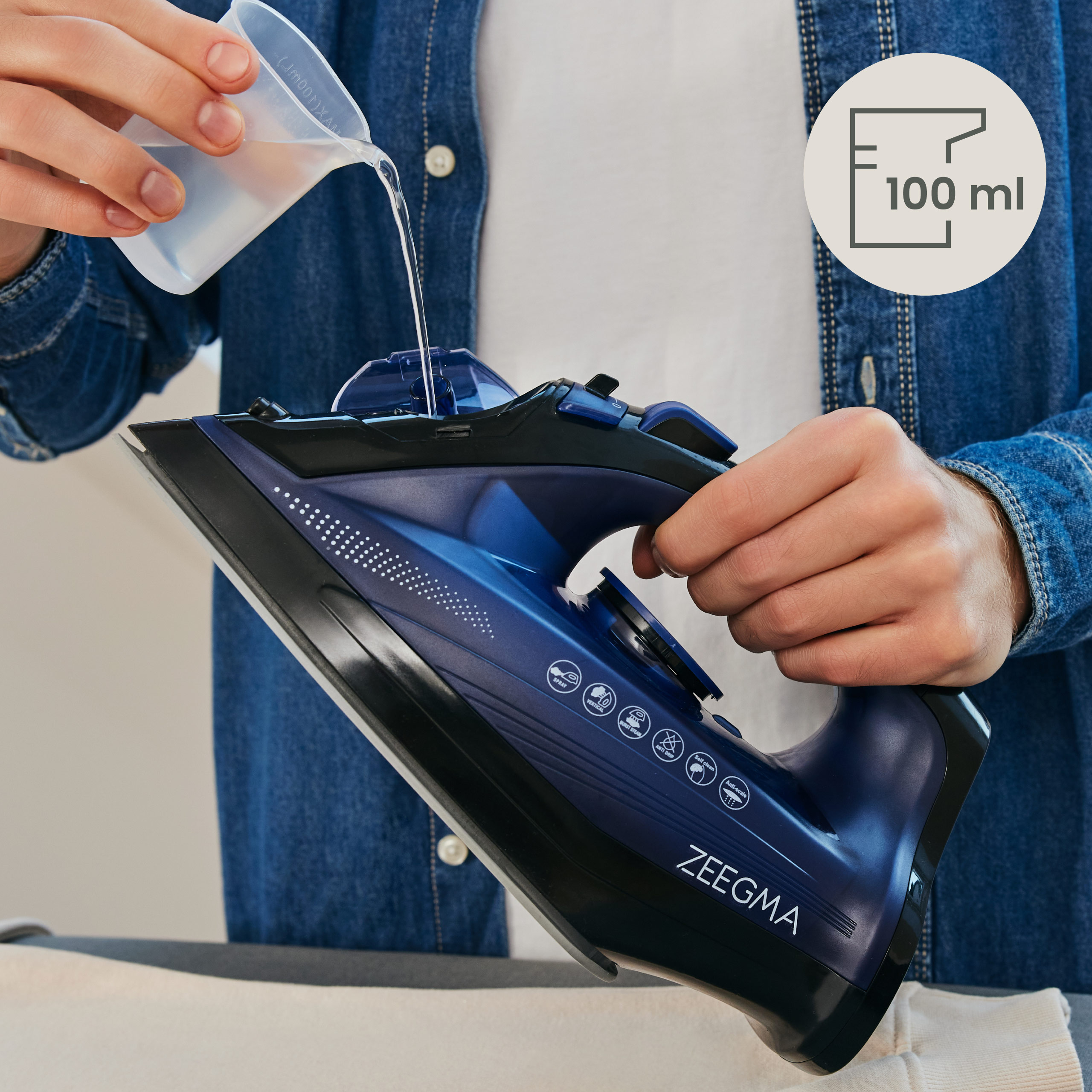 Osoba wlewa wodę do niebieskiego żelazka. W kadrze znajduje się wskaźnik 100 ml.