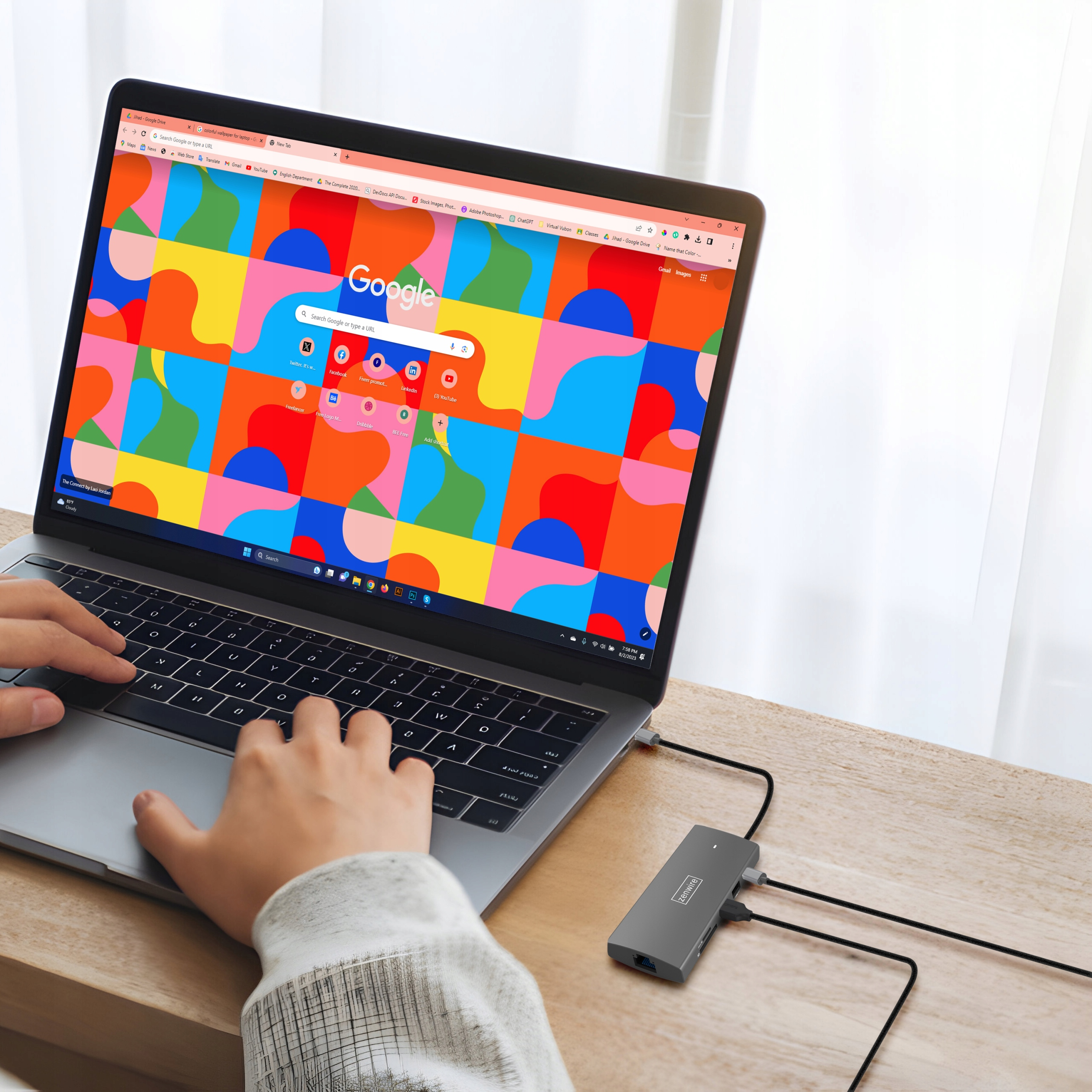Eine Person benutzt einen Laptop. Ein grauer Hub verbindet sich mit dem Laptop und einem Monitor. Ein farbenfroher Hintergrund.