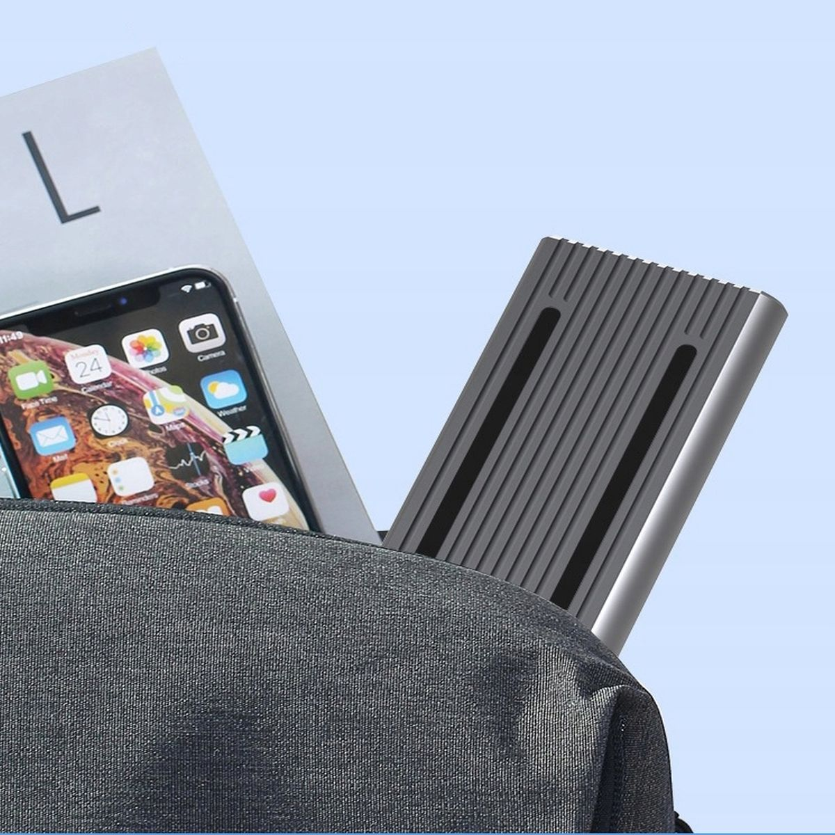 Tablet w kieszeni plecaka, obok telefonu i kartki papieru. Tło jest jasnoniebieskie.