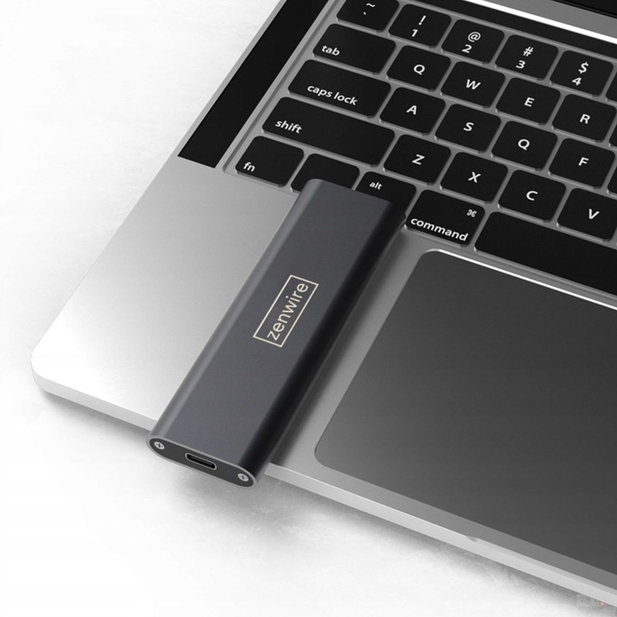 Eine graue externe SSD liegt auf einem Laptop. Sie hat ein silbernes Logo und einen USB-C-Anschluss.
