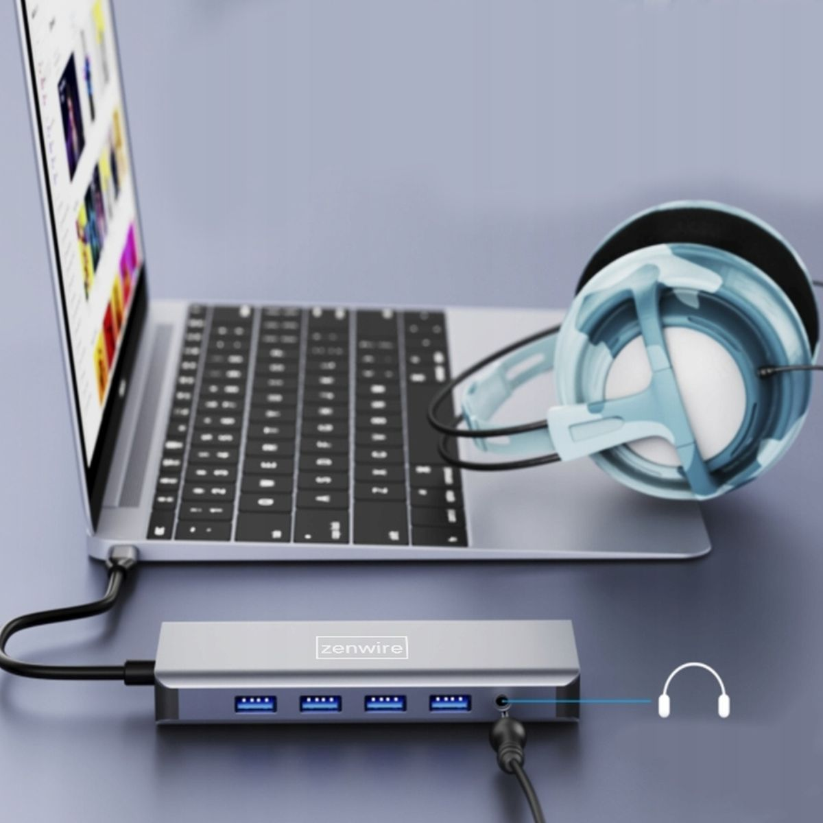 Laptop podłączony do srebrnego huba USB. Słuchawki leżą obok. Niebieskie tło.
