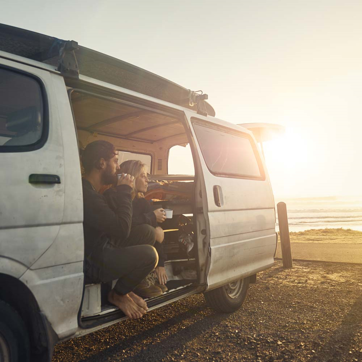 Paar in einem Van am Strand. Die Sonne geht unter. Van-Tür offen.