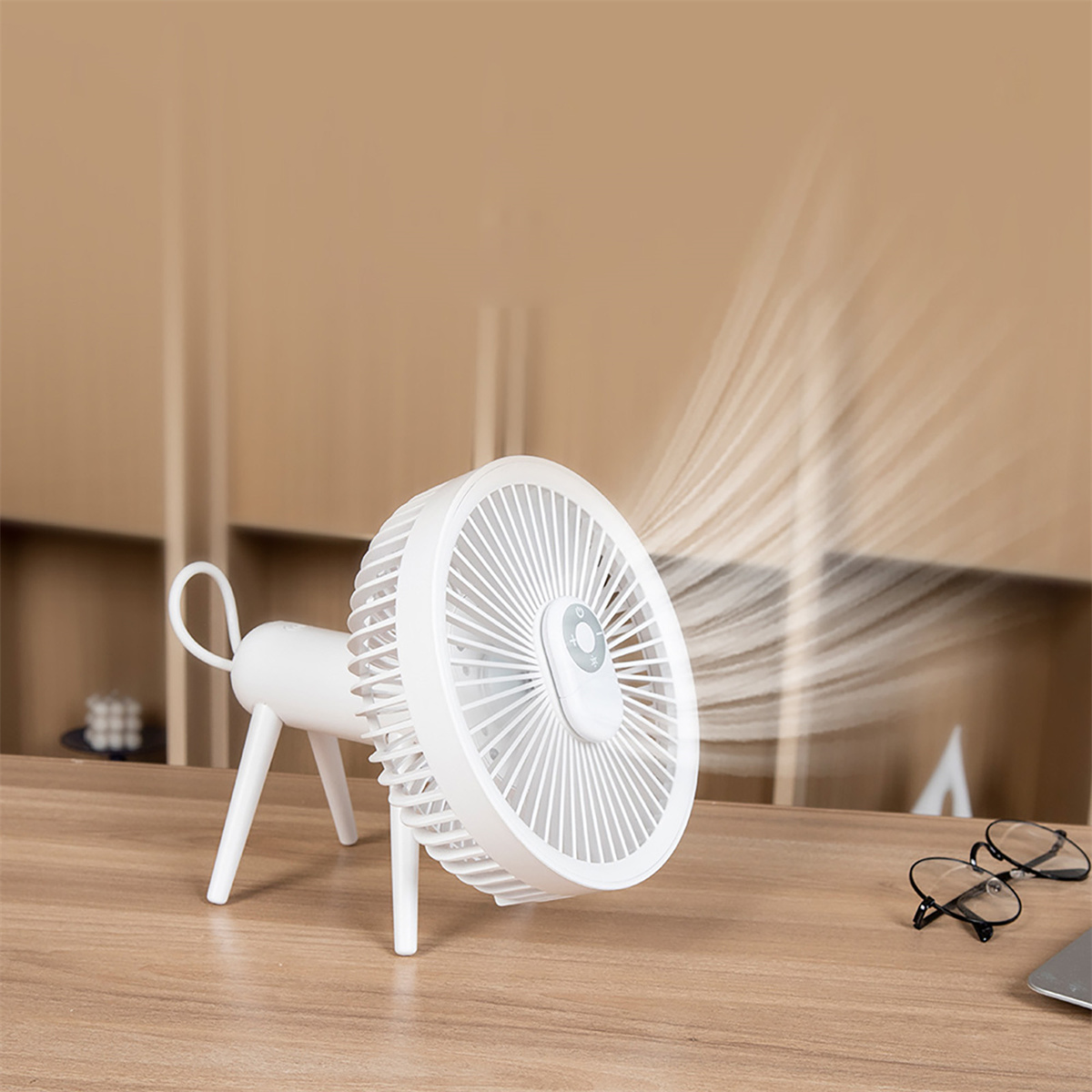 Weißer Schreibtischventilator mit drei Beinen, der Luft bläst. Hintergrund ist ein Holztisch.