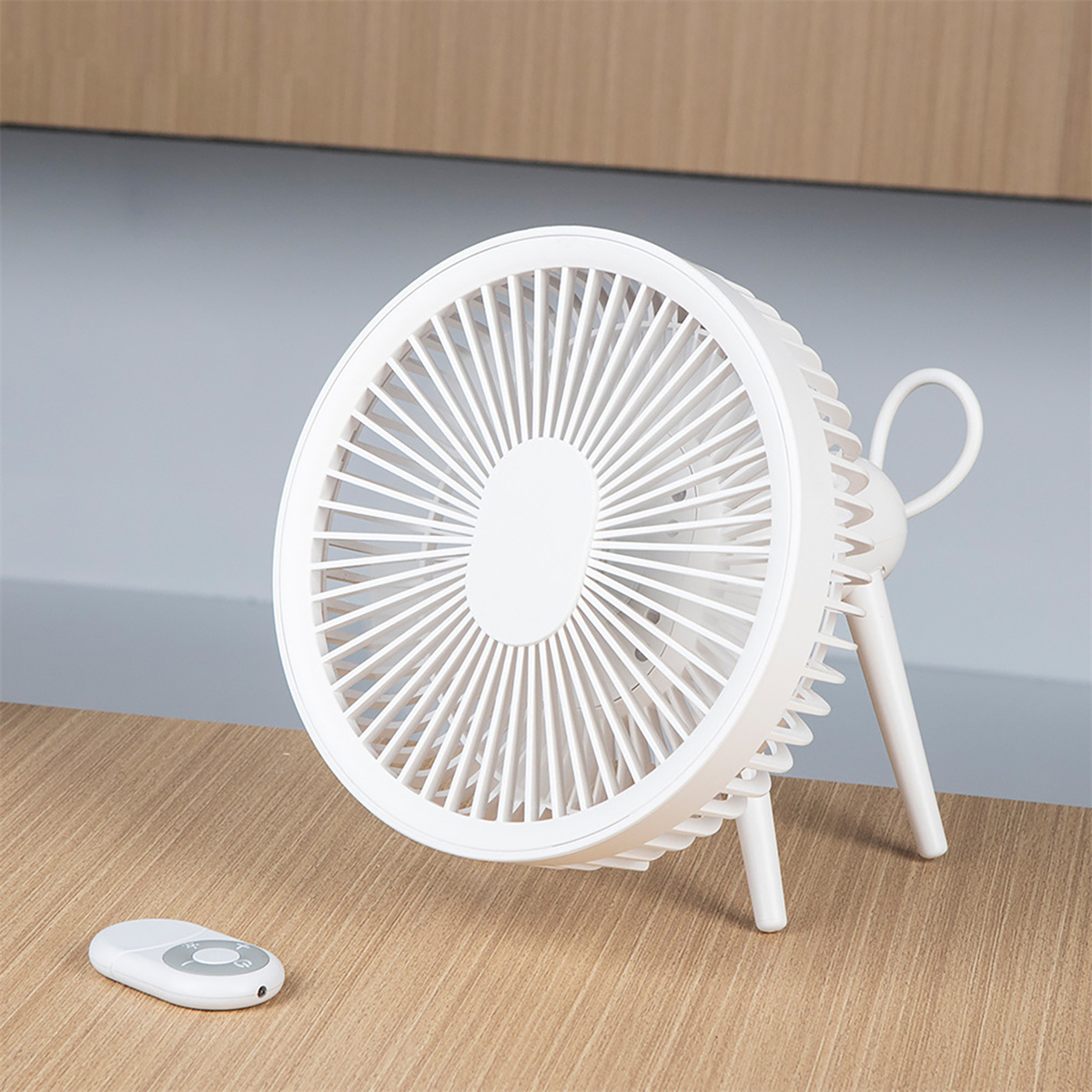 Weißer Schreibtischventilator mit Fernbedienung auf einem Holztisch und grauem Hintergrund.