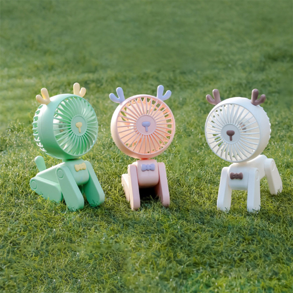 Drei hirschförmige Ventilatoren in Grün, Rosa und Weiß auf Gras.