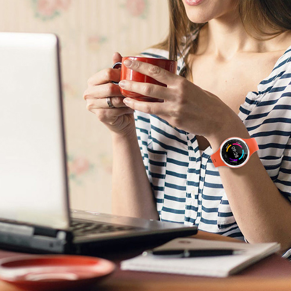 Eine Frau mit Smartwatch, die einen Laptop benutzt und einen roten Becher hält.