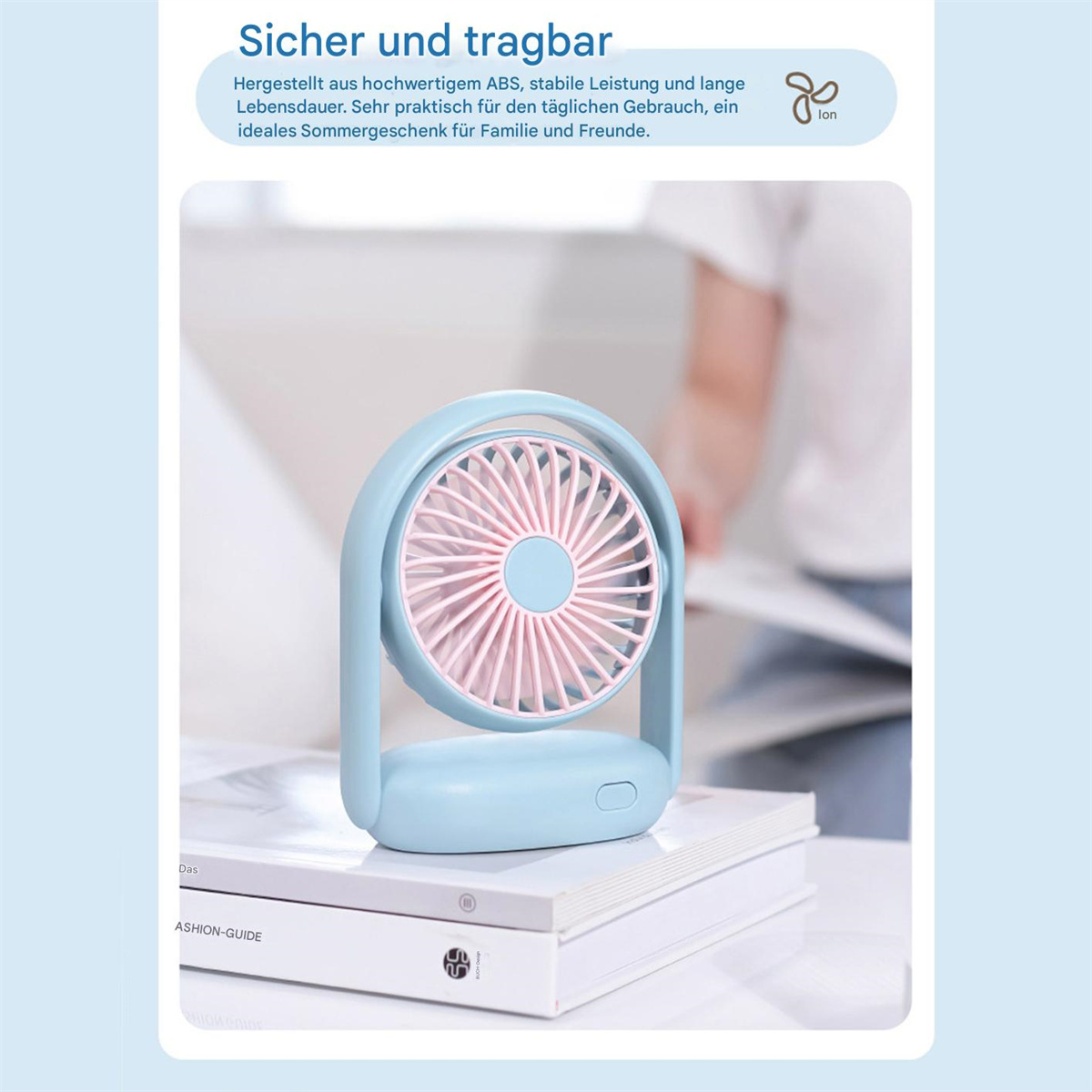 Ein blau-rosa tragbarer Ventilator liegt auf Büchern. Text auf Deutsch: 'Sicher und tragbar'.