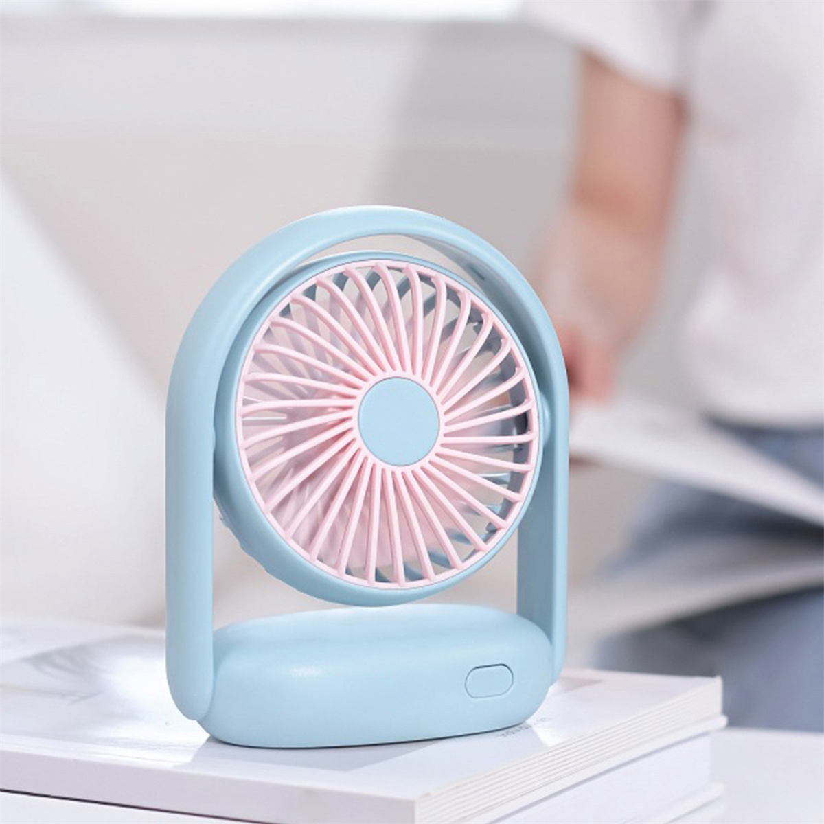 Kleiner blauer Ventilator mit rosa Flügeln, auf einem Buch platziert. Verschwommener Hintergrund.