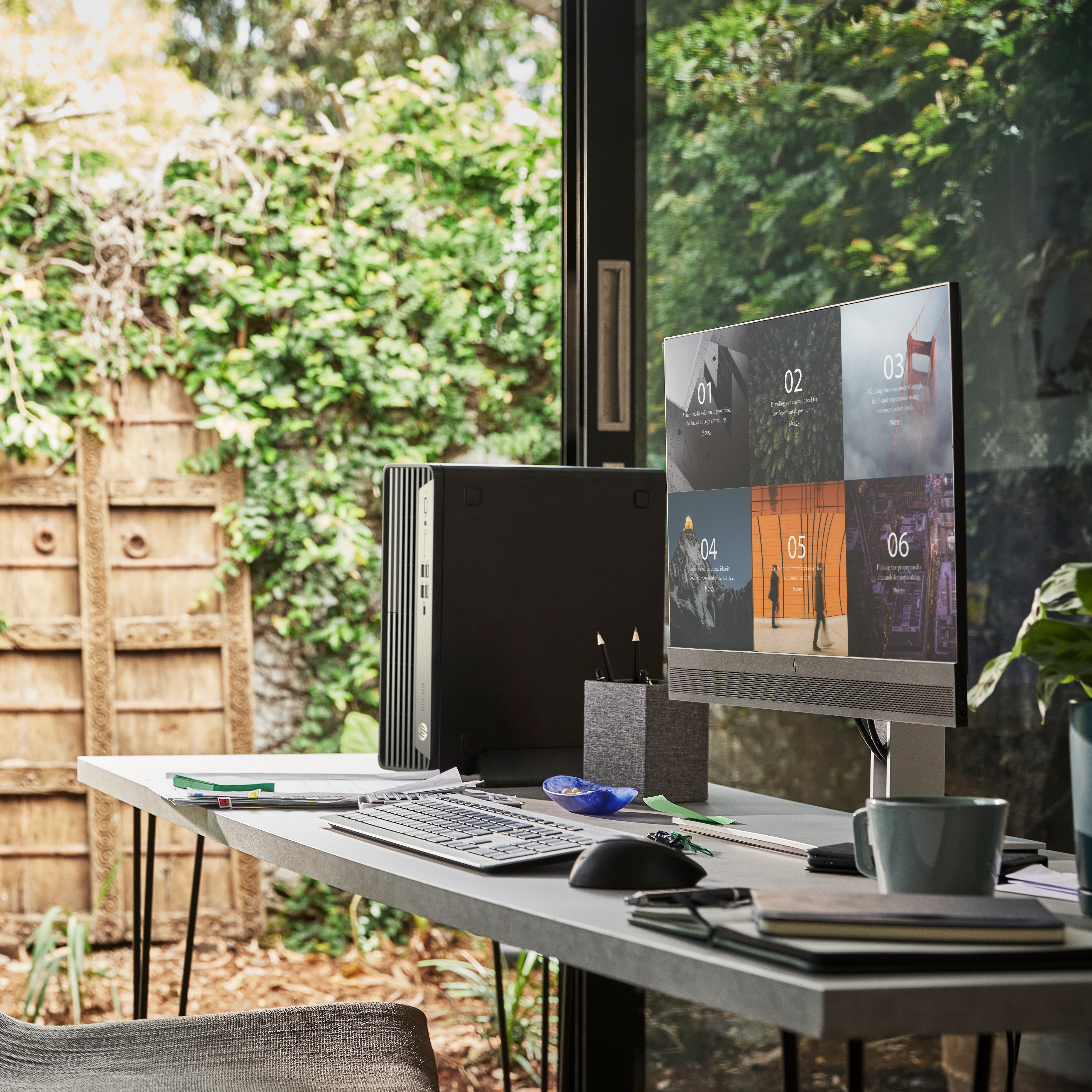 Biurko z komputerem, monitorem, klawiaturą i tłem z roślinami.