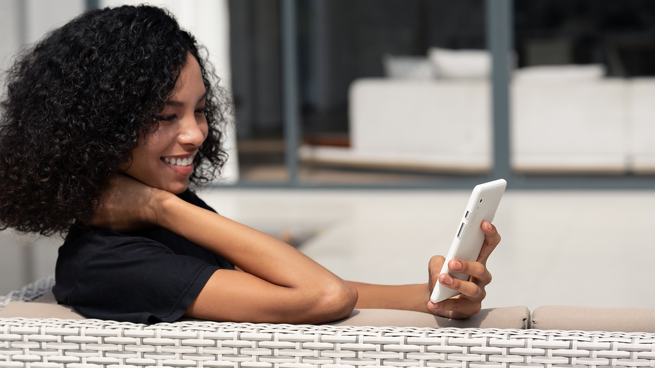 Kobieta z kręconymi włosami uśmiecha się trzymając biały tablet na zewnątrz.
