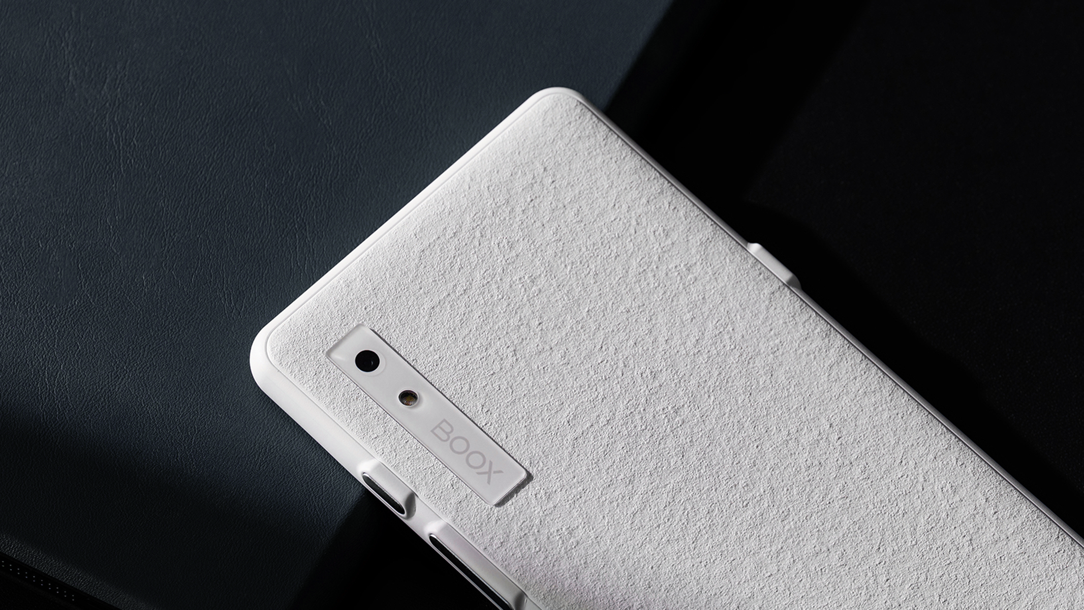 Biały telefon z teksturowanym tyłem, aparatem i logo BOOX, leżący na ciemnej powierzchni.