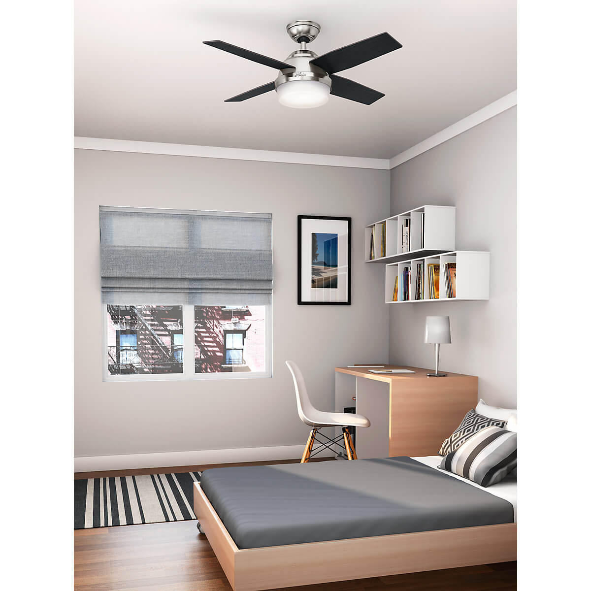 Schlafzimmer mit Deckenventilator. Fenster, Schreibtisch mit Lampe, Bett und Kunstwerk. Grau, Weiß und Schwarz dominieren.